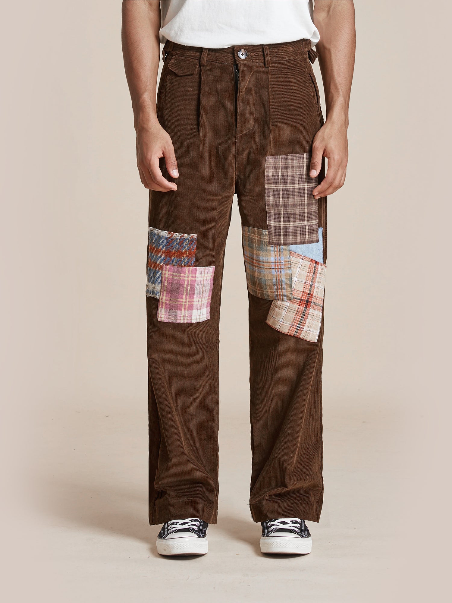 A person standing wearing Found Multi-Plaid Patch Corduroy Pants with multi-plaid patch detail on the thighs, paired with white and black sneakers.