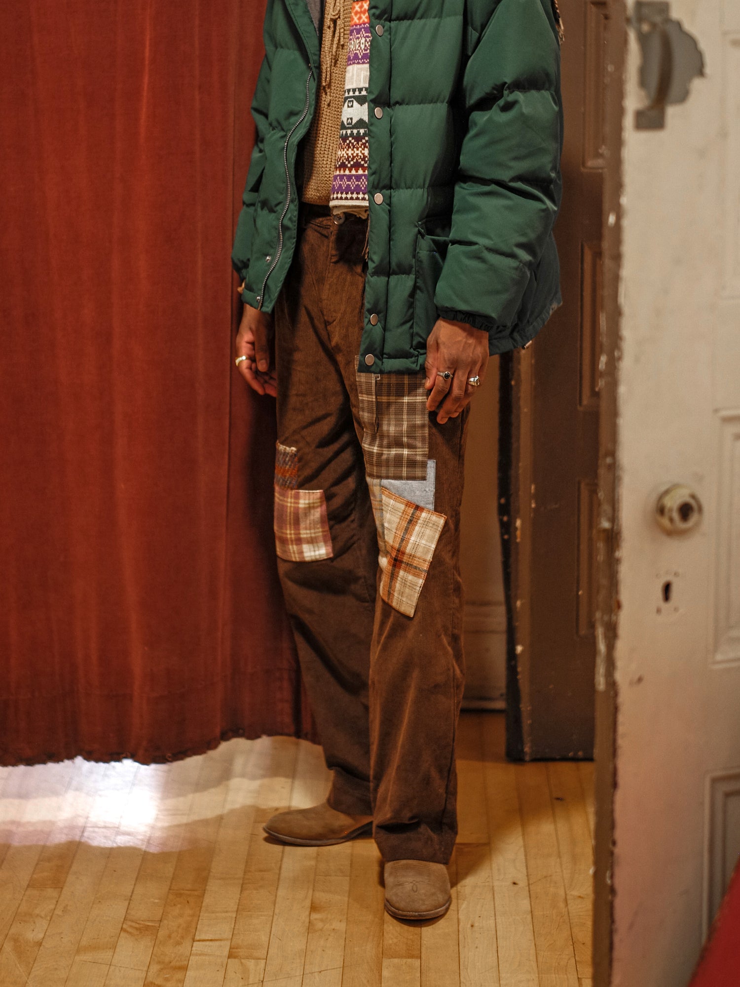 A man in a green jacket, wearing Found Multi-Plaid Patch Corduroy Pants, standing next to a door.