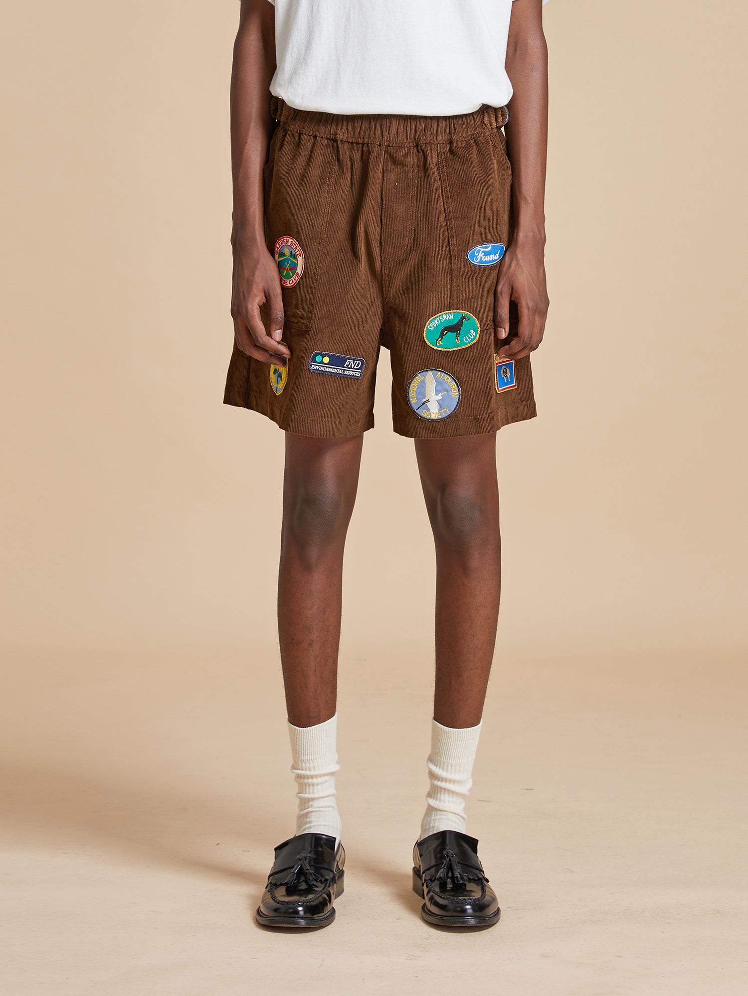 A man in brown Canoe Multi Patch Corduroy Shorts by Found.