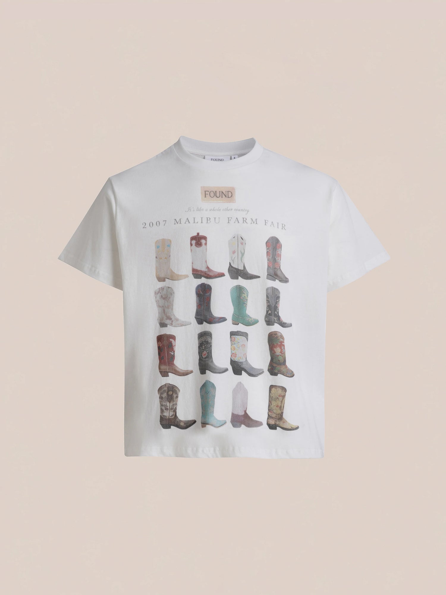 The Malibu Farm Fair Tee by FOUND is a white t-shirt made from 100% cotton fabric, featuring an array of colorful cowboy boots organized in a grid pattern. It displays the text 