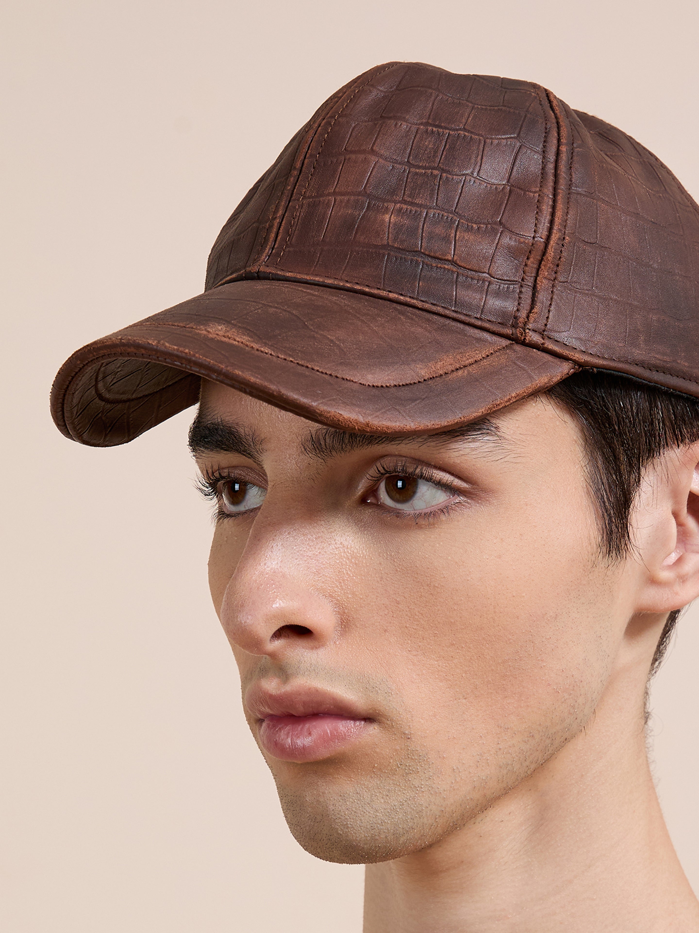 A person models the Found Croc Embossed Distressed Leather Cap, shown from the front and side against a plain beige background. The cap features brown crocodile-embossed leather and an adjustable fit.