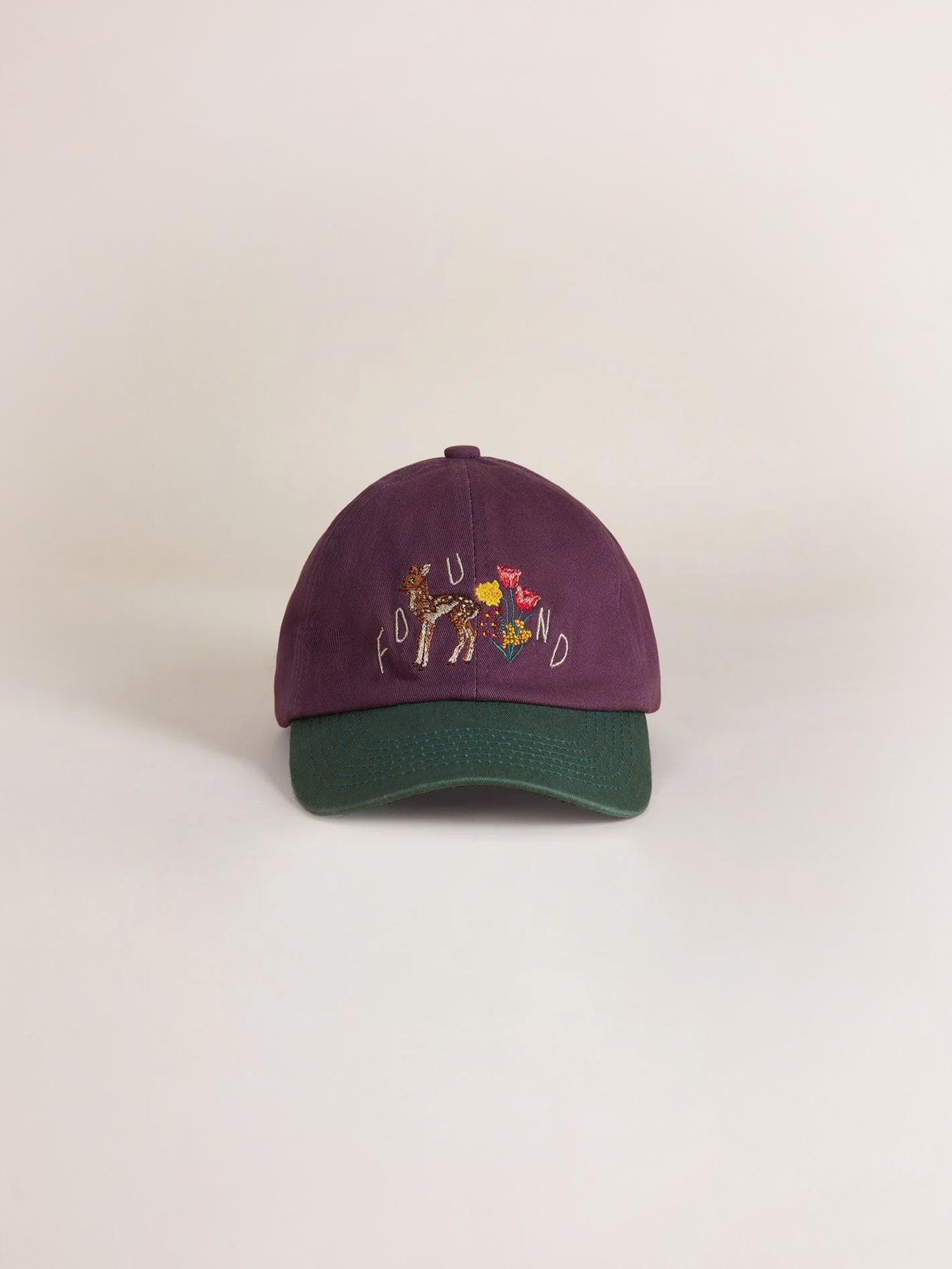 The Flower Deer Cap by Found is a purple and green baseball cap featuring an intricately embroidered design of a giraffe, flowers, and the brand name 