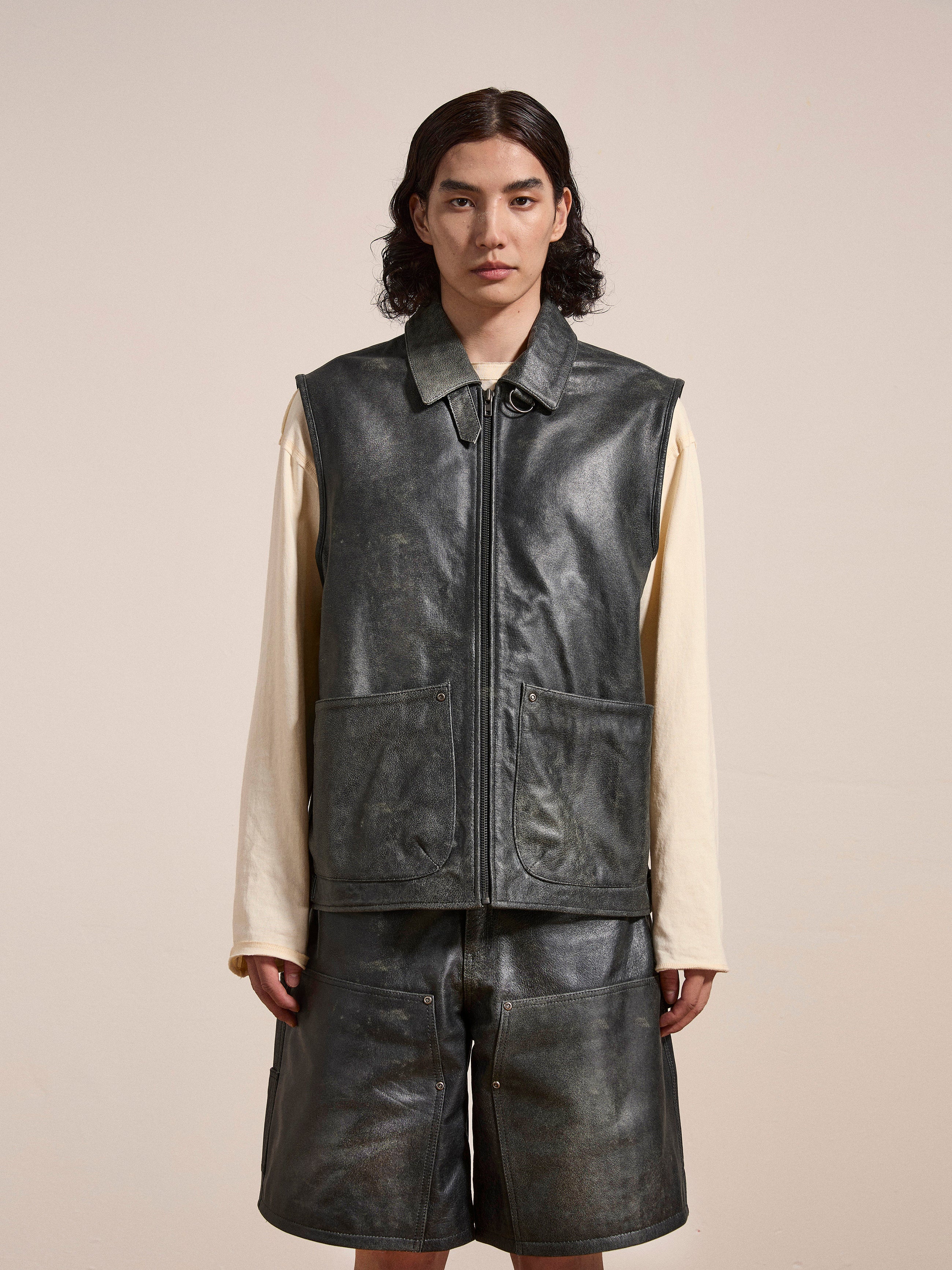 A person with shoulder-length hair is wearing an ethically sourced Found Distressed Genuine Leather Pocket Vest over a long-sleeve shirt and matching leather shorts.