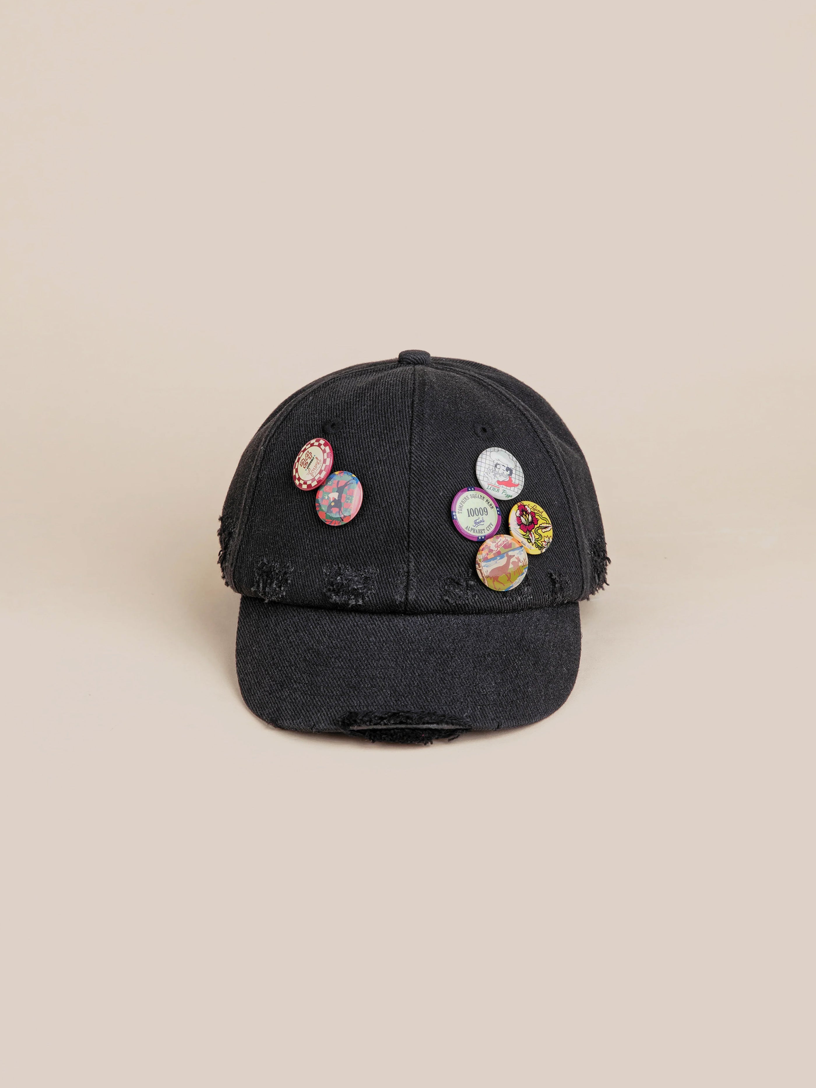 The FOUND Distressed Pin Cap is made from 100% cotton, showcasing frayed edges and embellished with six colorful, vintage-inspired pins on the front.