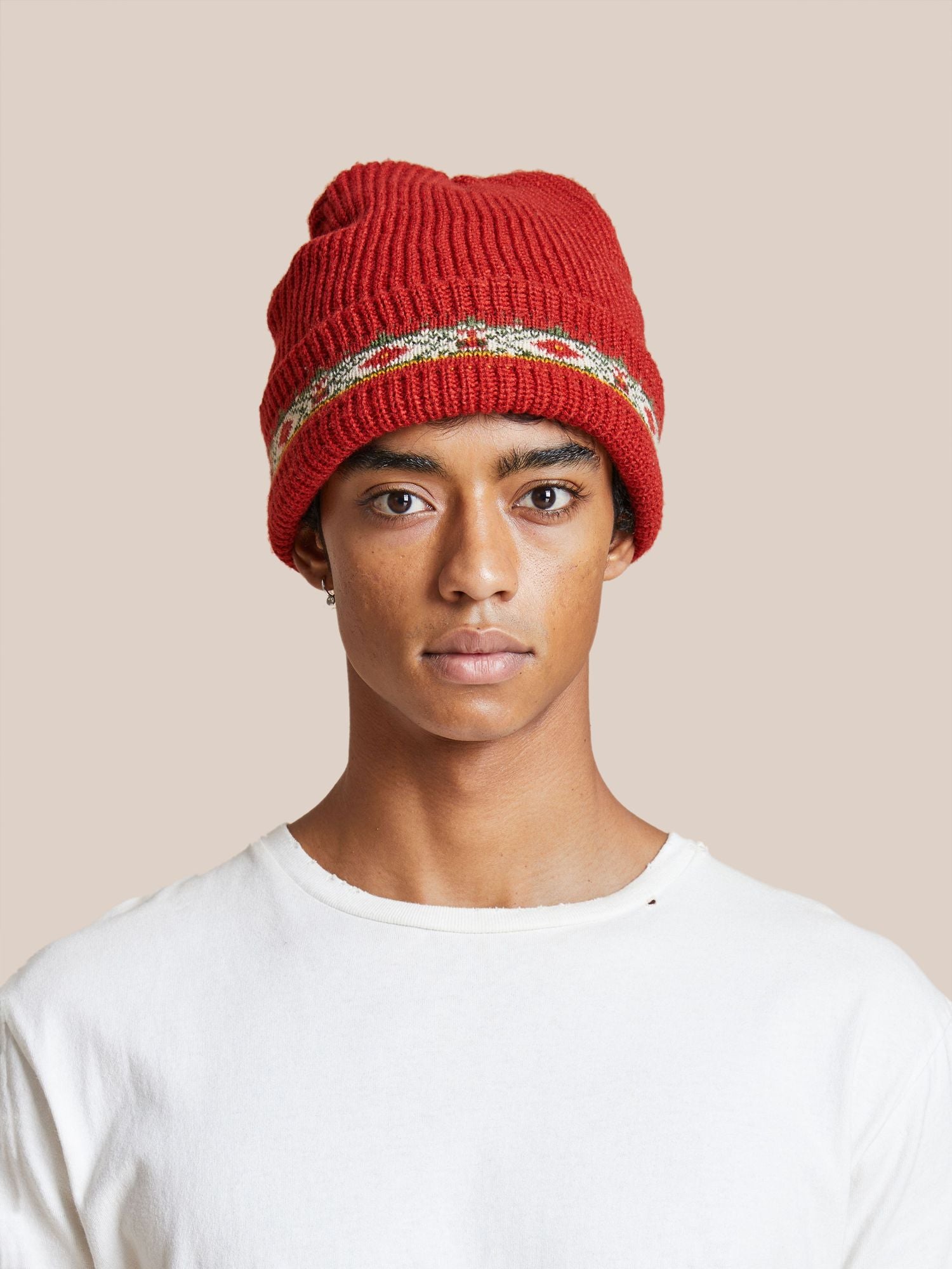 Young man wearing a Profound Ajrak Beanie and white t-shirt, facing directly towards the camera with a neutral expression, against a beige background.
