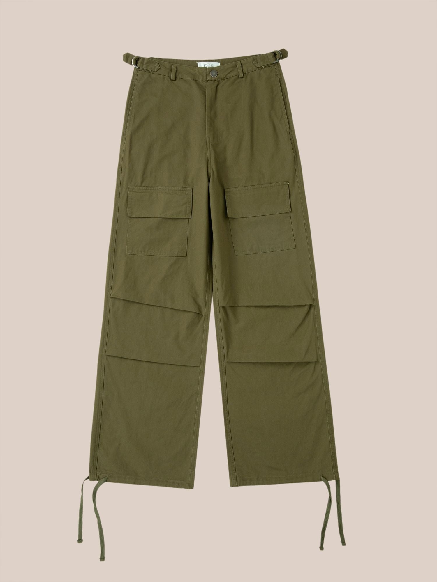 Olive green Found parachute cargo twill pants with multiple pockets and drawstrings at the ankles against a pink background.
