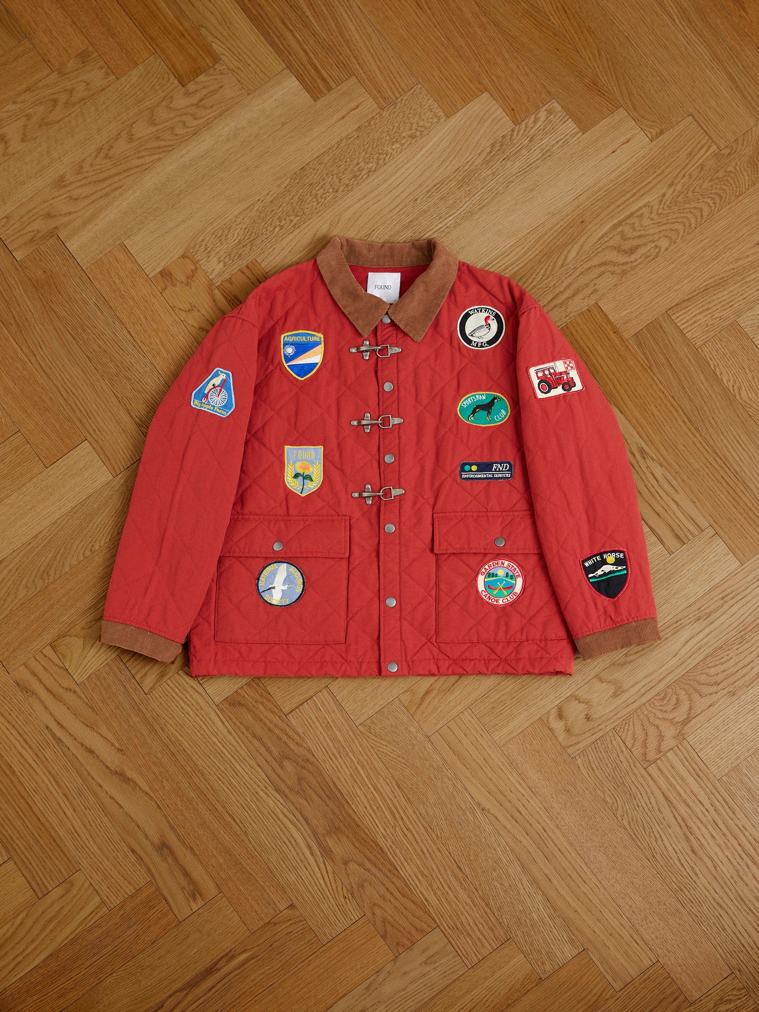 A red Found Farmstead Quilt Patch Jacket with multiple colorful patches and a corduroy collar laid flat on a wooden floor.