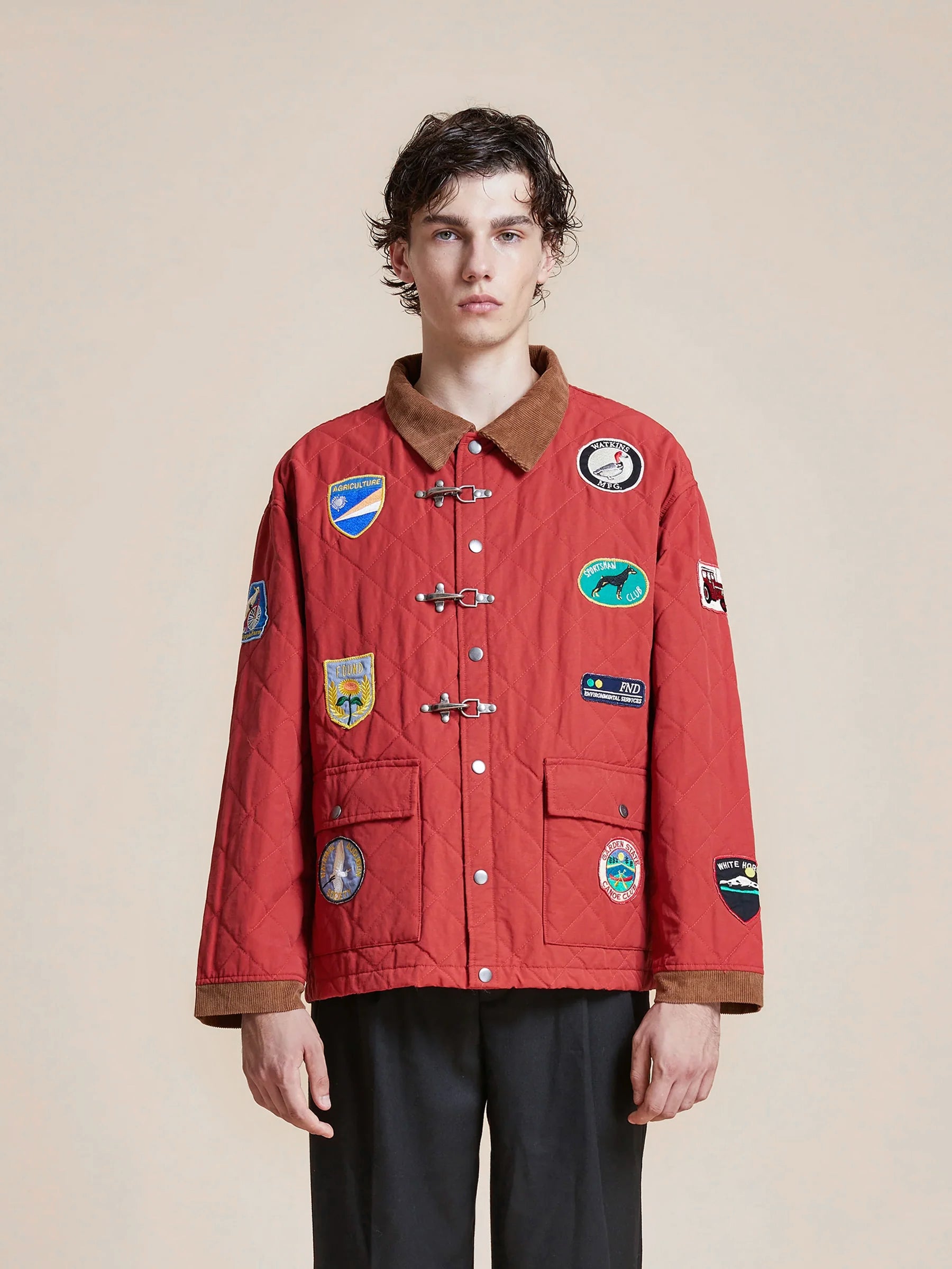 A young man wearing a Found Farmstead Quilt Patch Jacket with various embroidered badges and a brown collar, standing against a neutral background.