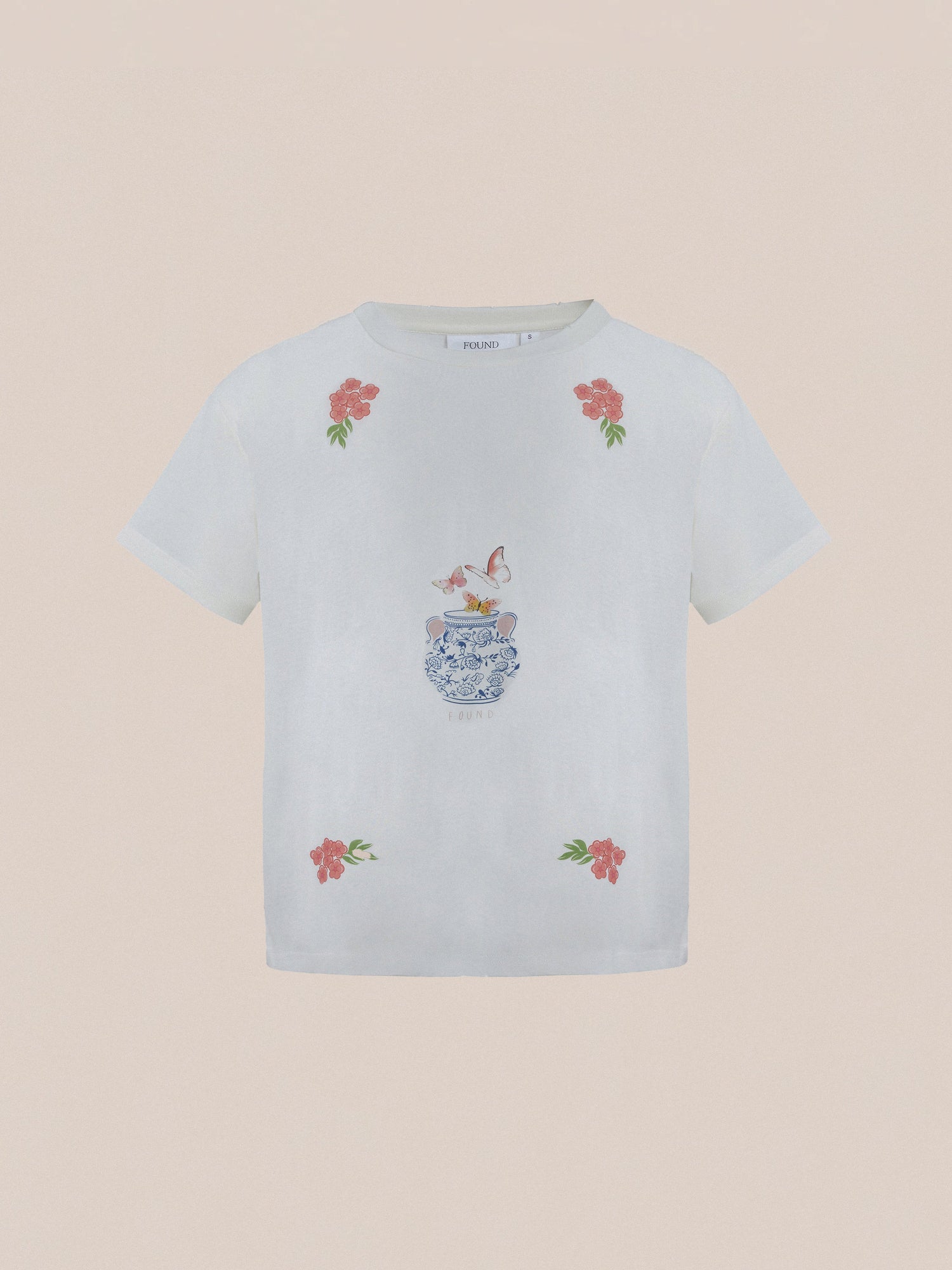 The Flower Pot Tee by Found is a white T-shirt adorned with floral accents and a whimsical design of two birds perched on a decorative vase, exuding springtime charm.