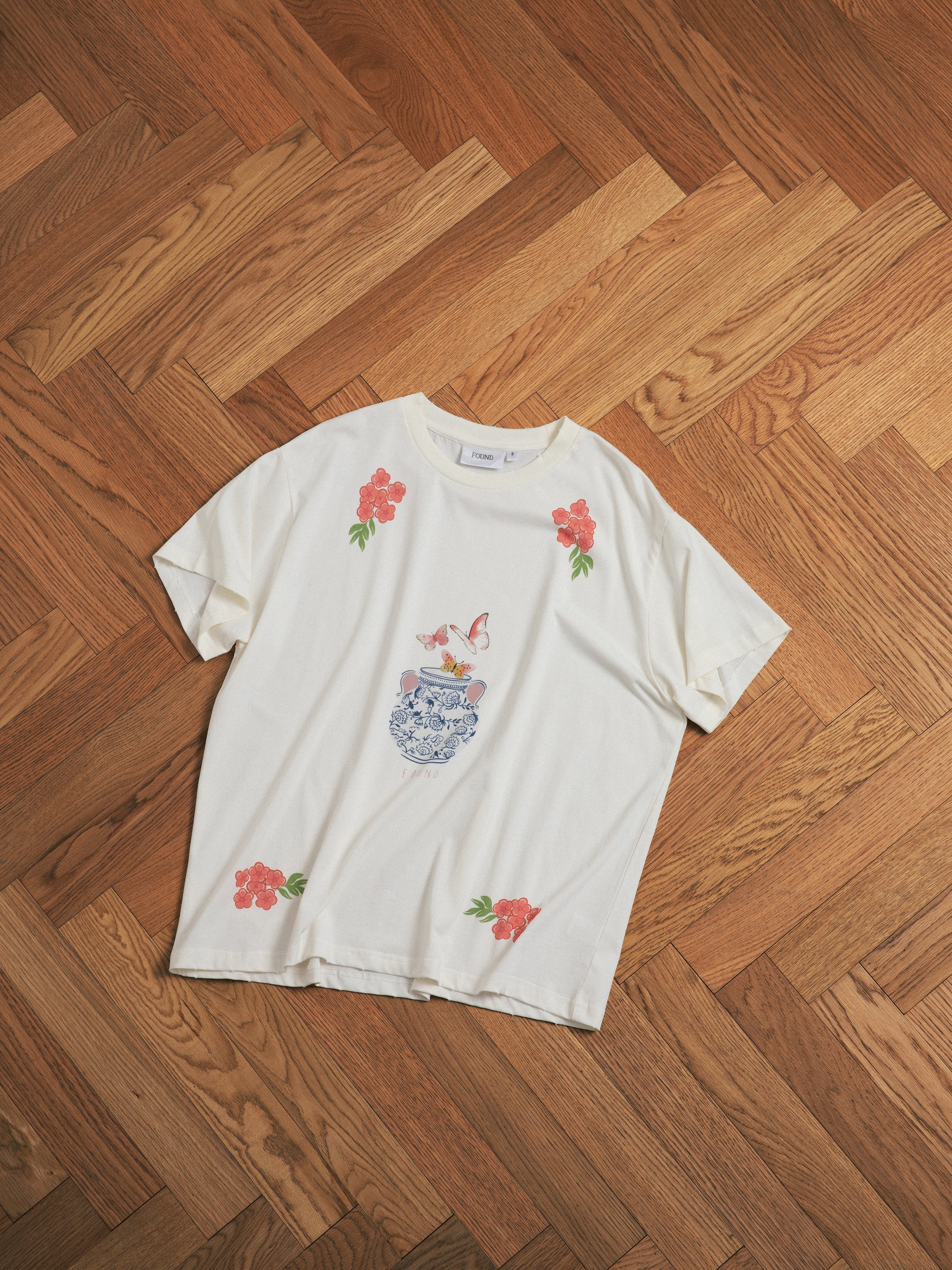 A Found Flower Pot Tee laying on a wooden floor.