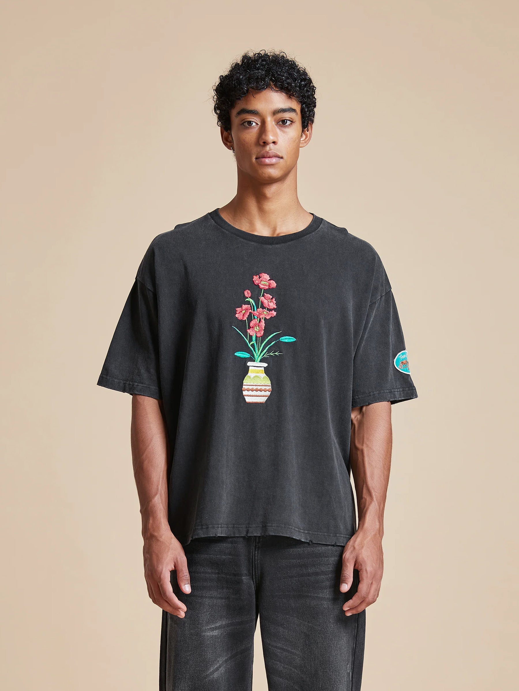 A man wearing a black t-shirt with a floral motif on it, called the Found Flowers Vase Tee.