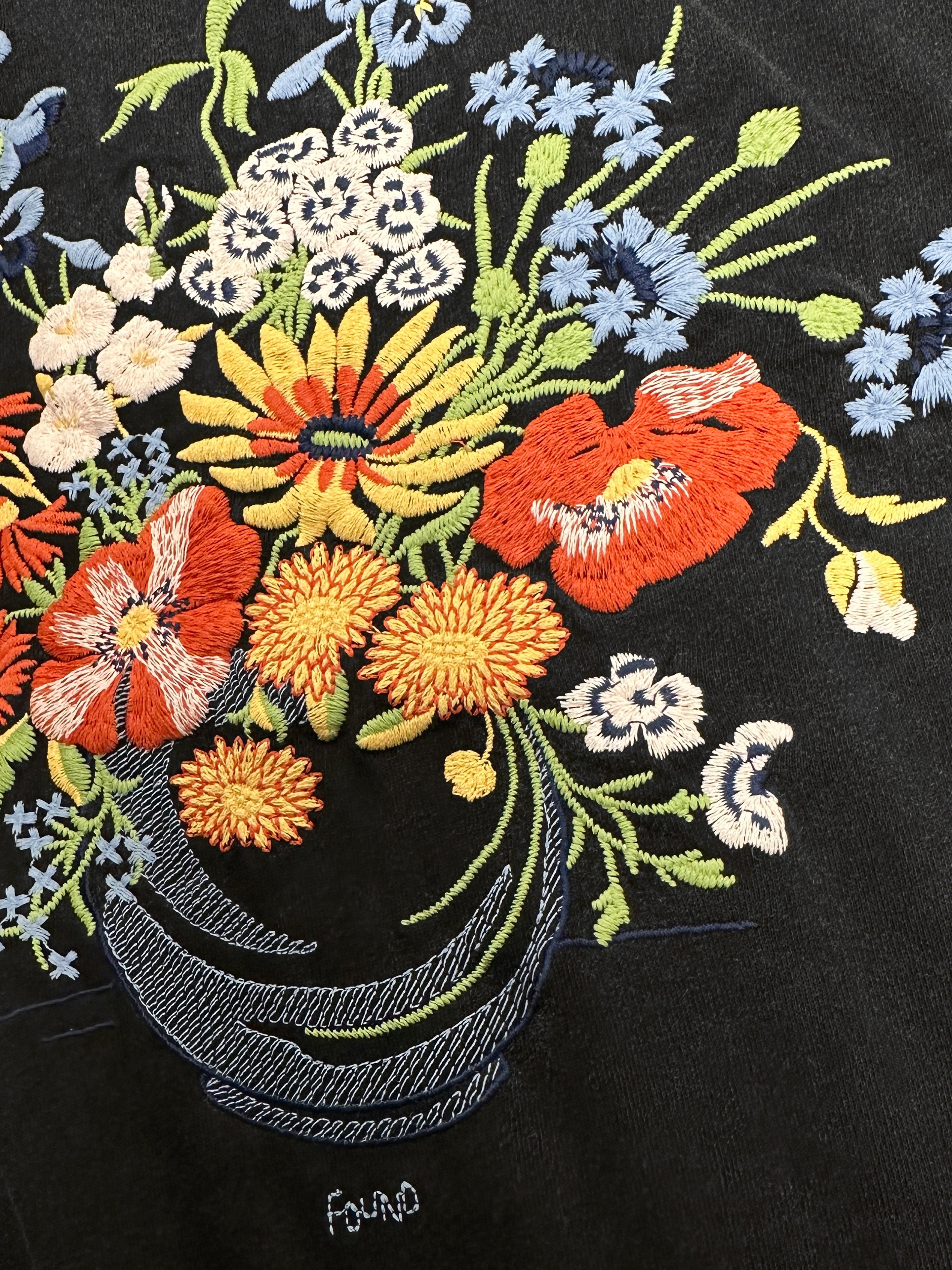 The Bouquet Flowers Tee by FOUND highlights Phulkari embroidery with a classic Punjab style, presenting an embroidered floral bouquet on black fabric embellished with red, yellow, and blue flowers, accented by green stems and leaves.