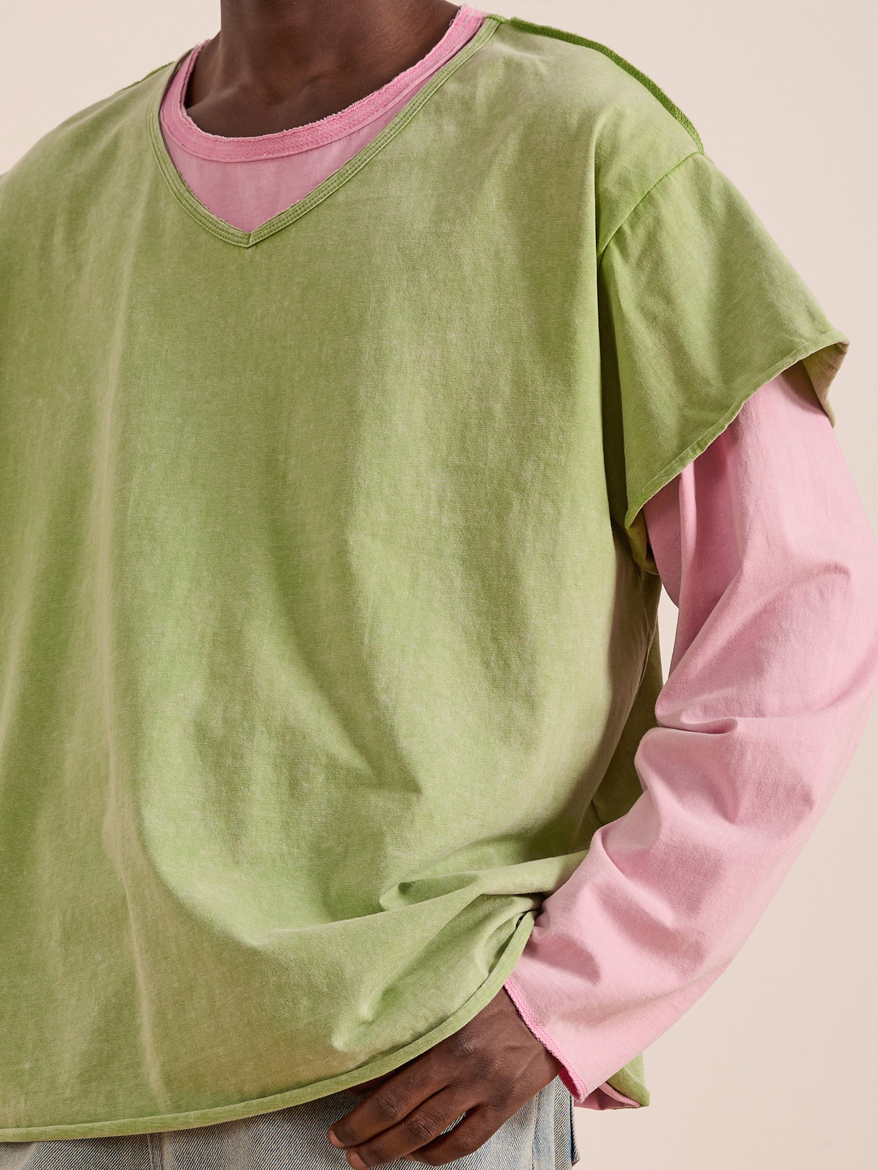 Model wears FOUND Double Layer LS Tee in light green sunfade wash layered over a long-sleeve pink shirt, paired with light-colored pants, shown from shoulders to hips against a plain background.