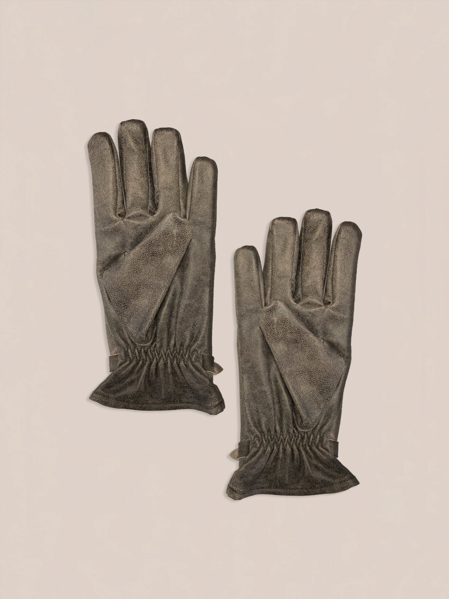 A pair of Distressed Leather Western Gloves by FOUND in gray with gathered cuffs on a light background.