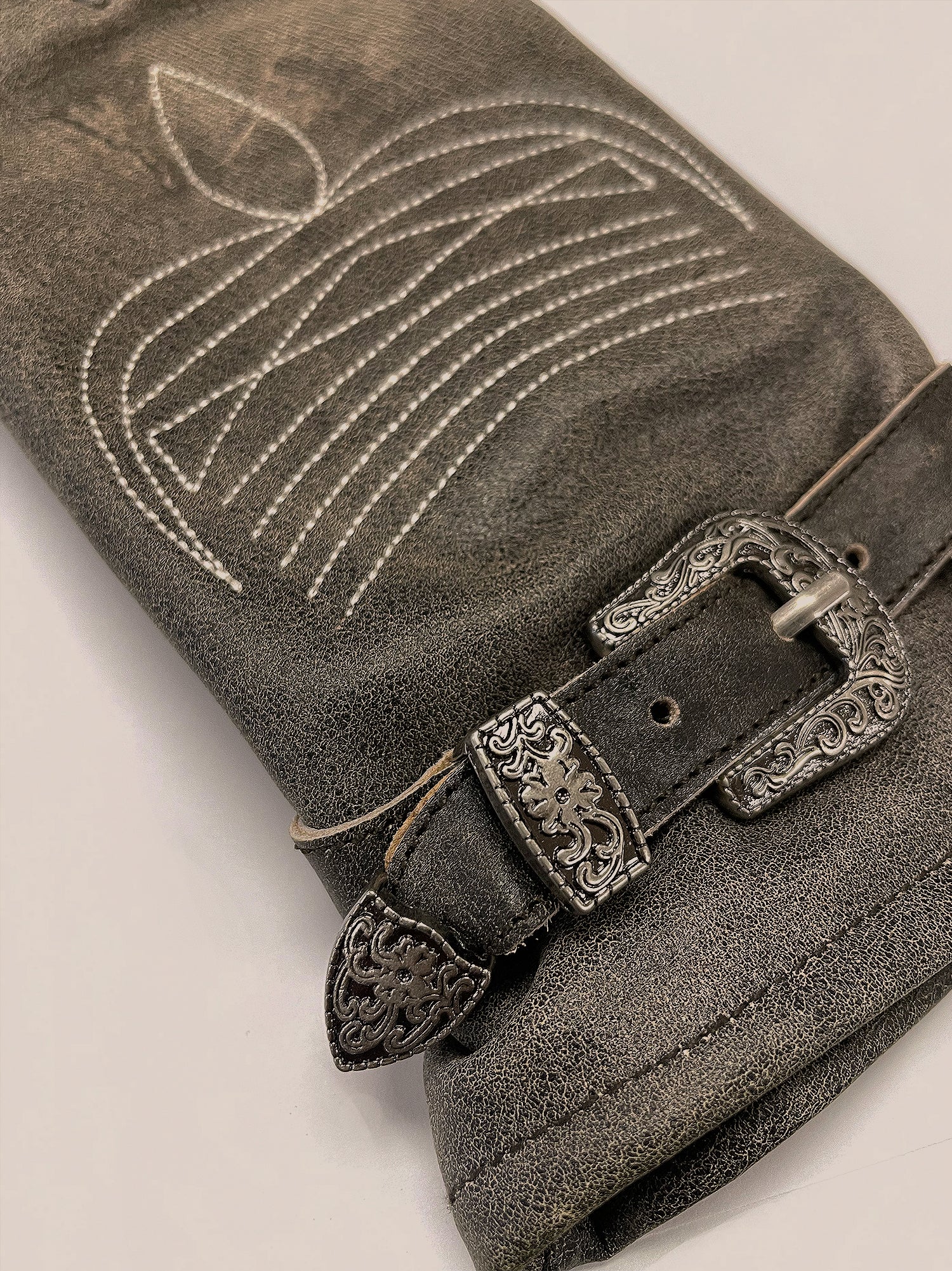 A pair of distressed leather western gloves from the brand FOUND rests on a gray textured surface with a stitched apple design.