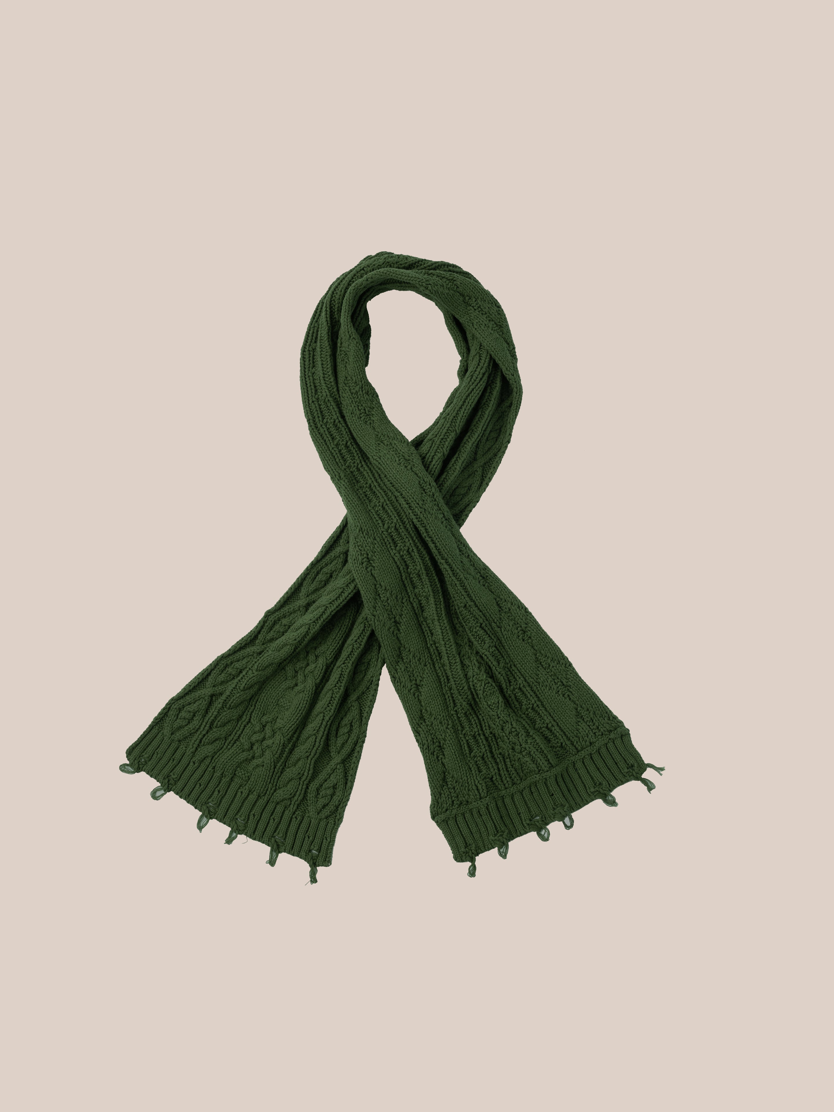 The Forest Distressed Cable Knit Scarf by FOUND, featuring an intricate cable pattern and small fringe ends, is elegantly displayed against a plain beige background.