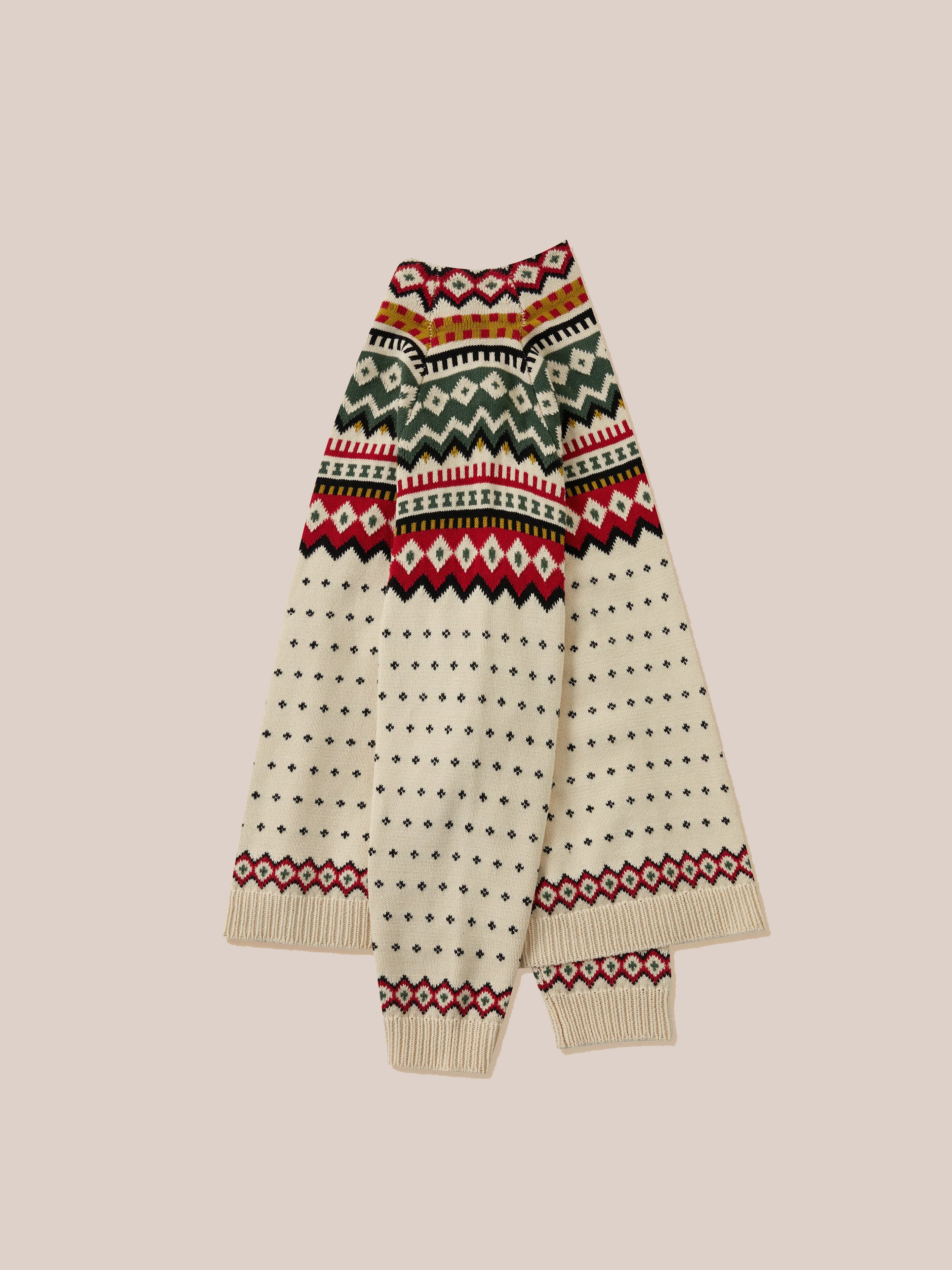 The Harwan Isles Sweater by Found showcases a folded cream design with vibrant geometric patterns in red, green, and black adorning the collar and cuffs, all set against a beige background. This iconic sweater embodies the essence of Scottish Fair Isle tradition.