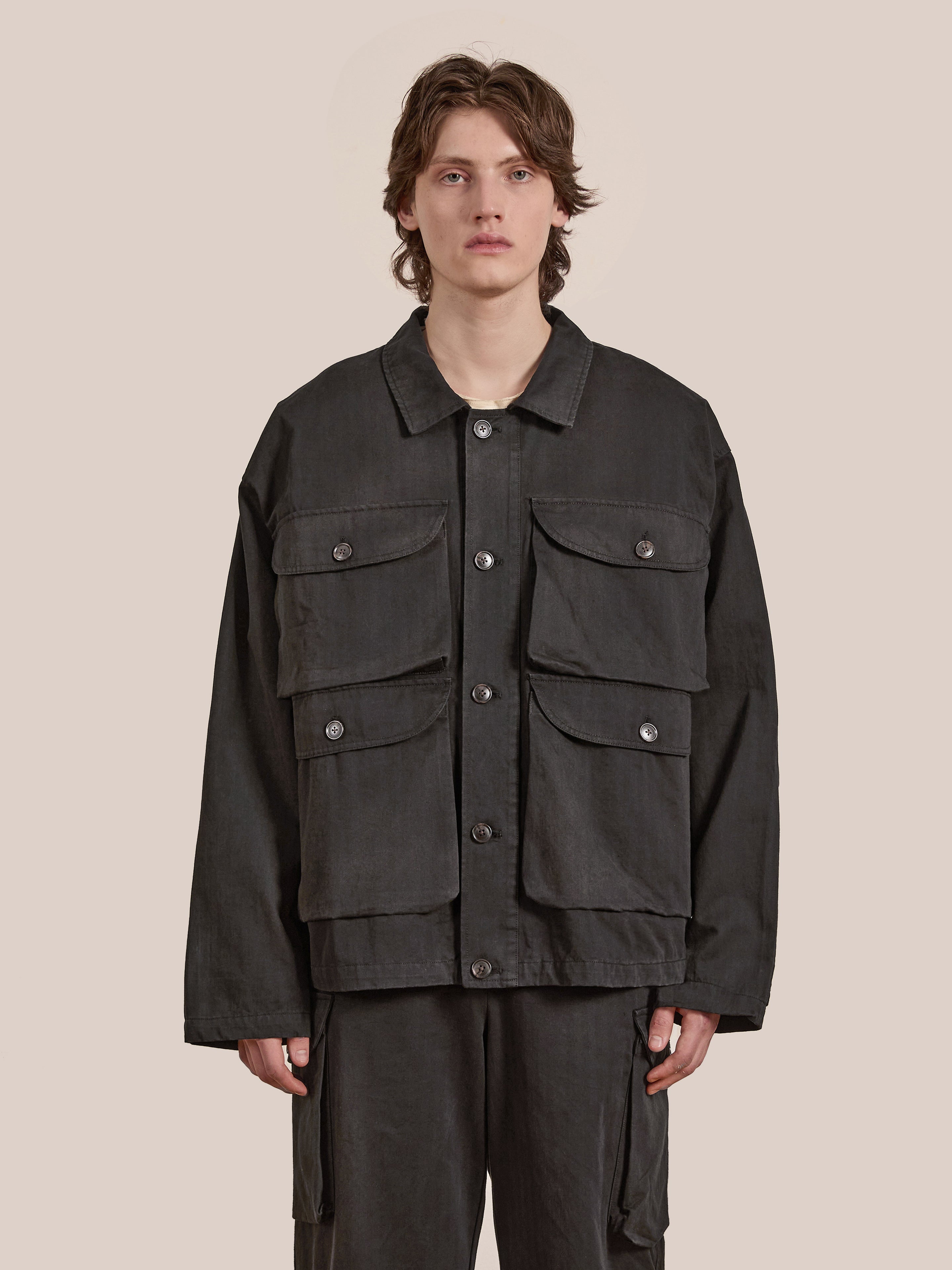 A person stands against a plain background wearing a Utility Herringbone Cargo Jacket with large pockets, made from cotton twill, by FOUND to complete the vintage look.