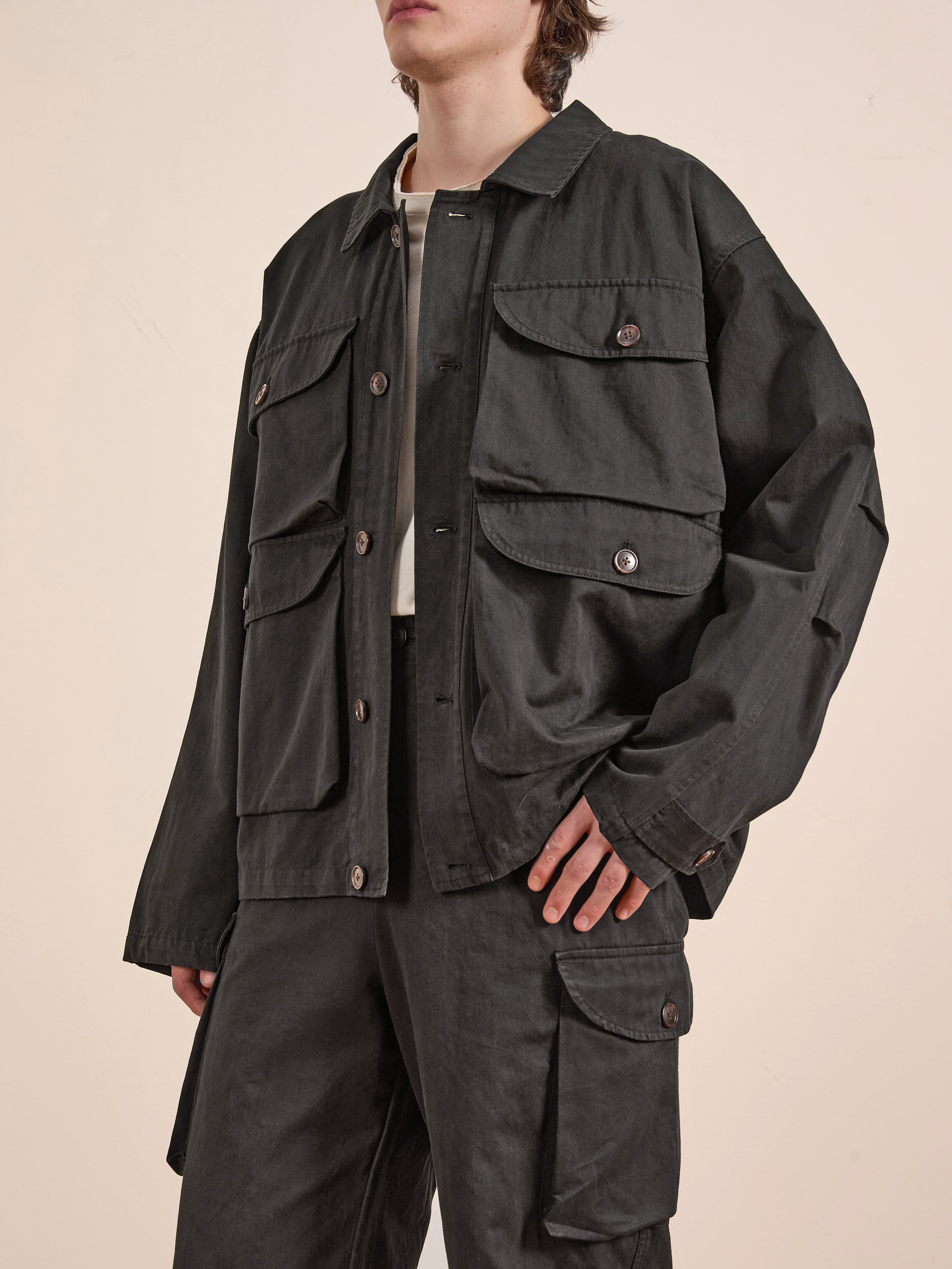 A person in a FOUND Utility Herringbone Cargo Jacket in dark green, featuring multiple pockets, paired with matching cargo pants, stands against a plain background.