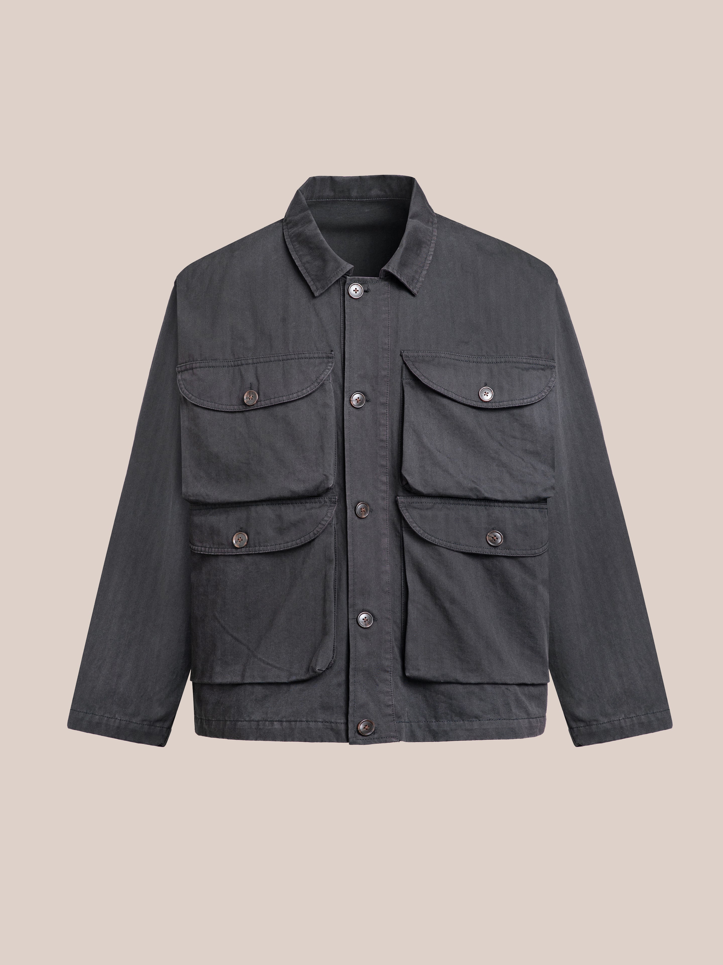 The Utility Herringbone Cargo Jacket by FOUND, in dark gray cotton twill with a vintage aesthetic, features four functional front pockets and is showcased on a beige background.