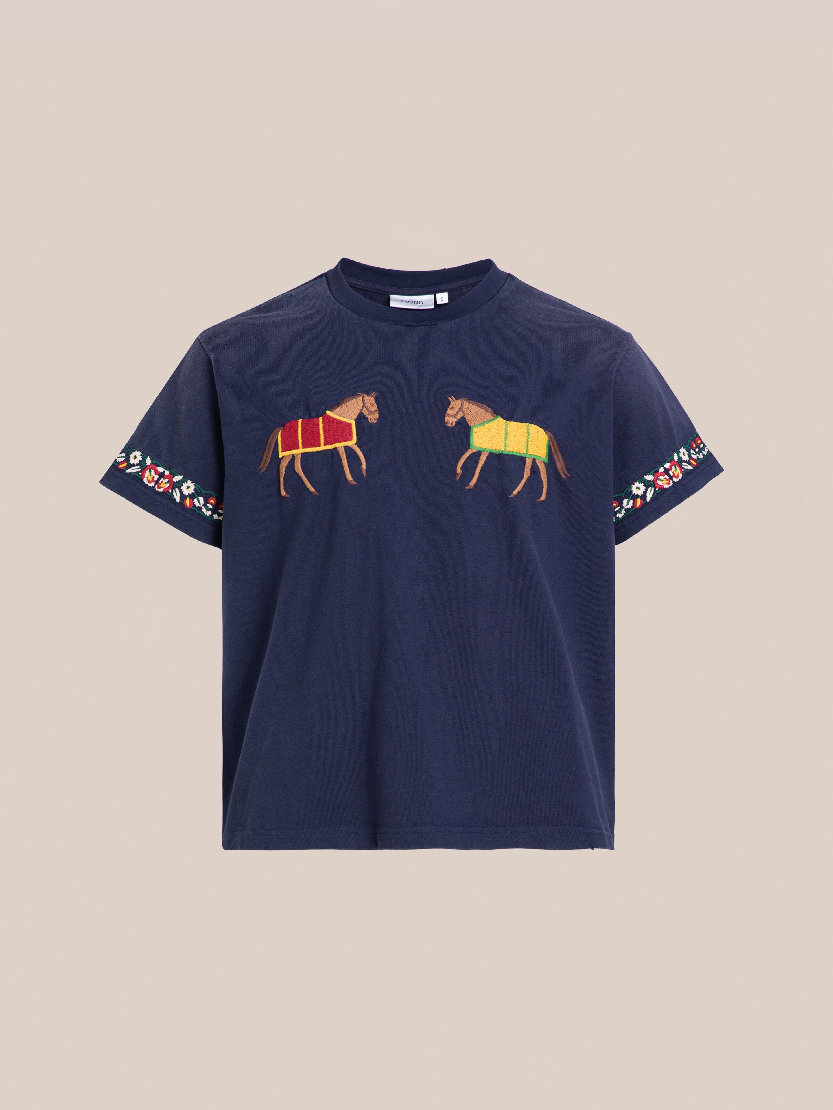 Check out the Horse Equine Tee by FOUND: a navy blue t-shirt featuring embroidered horses on the chest, one wearing a red blanket and the other a yellow blanket, complemented by floral patterned sleeves.