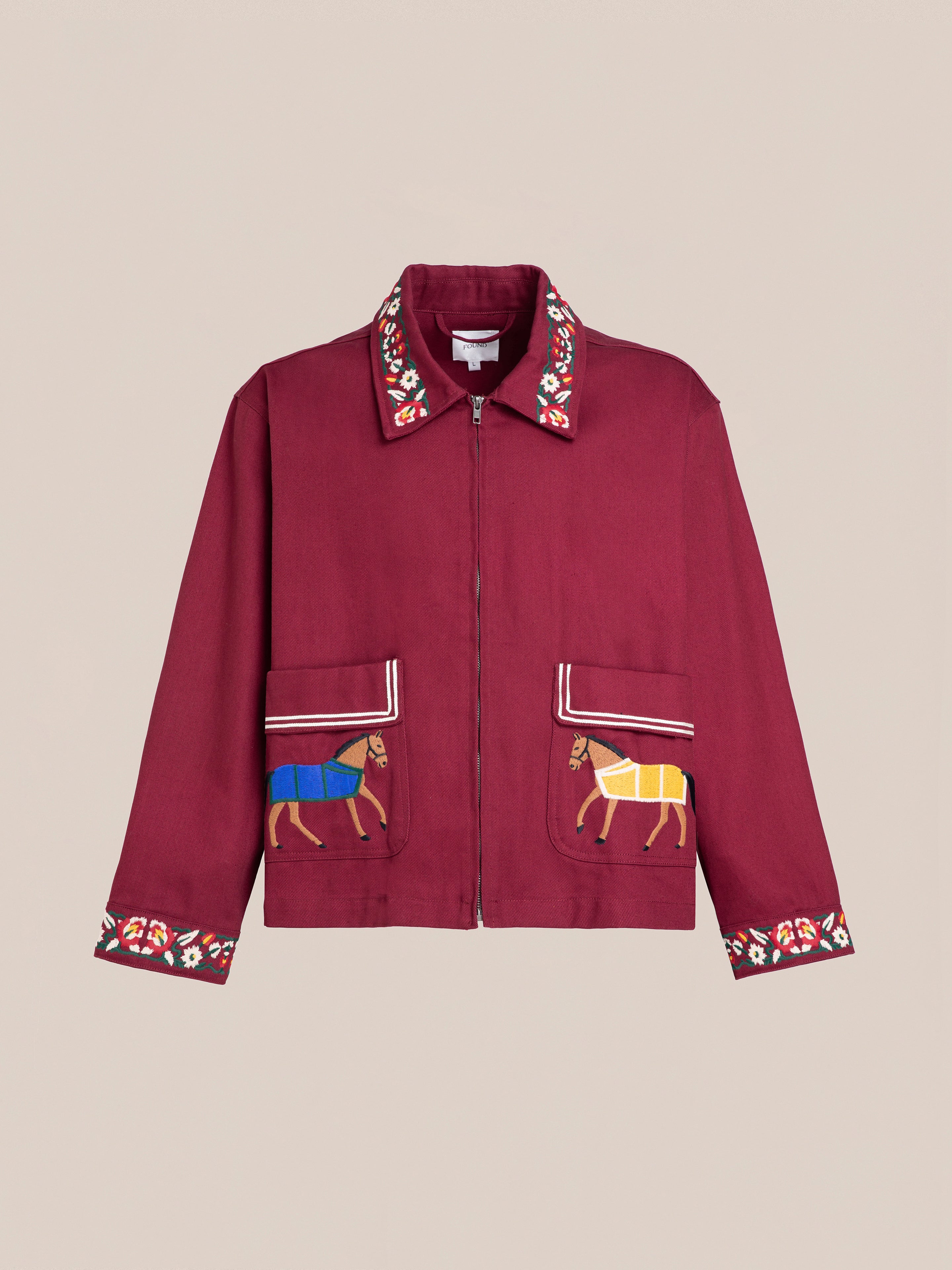 The Oxblood Horse Equine Jacket by FOUND features a front zipper and is adorned with embroidered trim on the collar, cuffs, and two front pockets. Reminiscent of 70's jockey uniforms, this lightweight cotton twill jacket showcases colorful embroidered horse designs on the pockets.