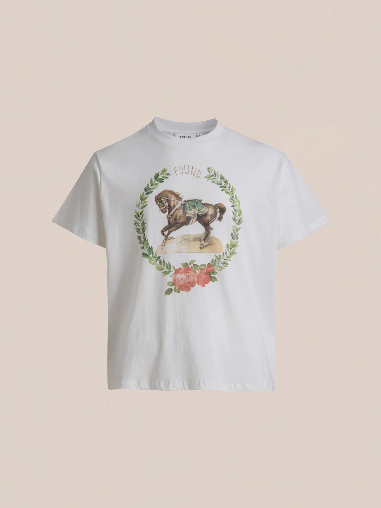 A white Rodeo Tee from the brand FOUND, adorned with a horse graphic encircled by a wreath of leaves and flowers for a vintage feel, and the word 