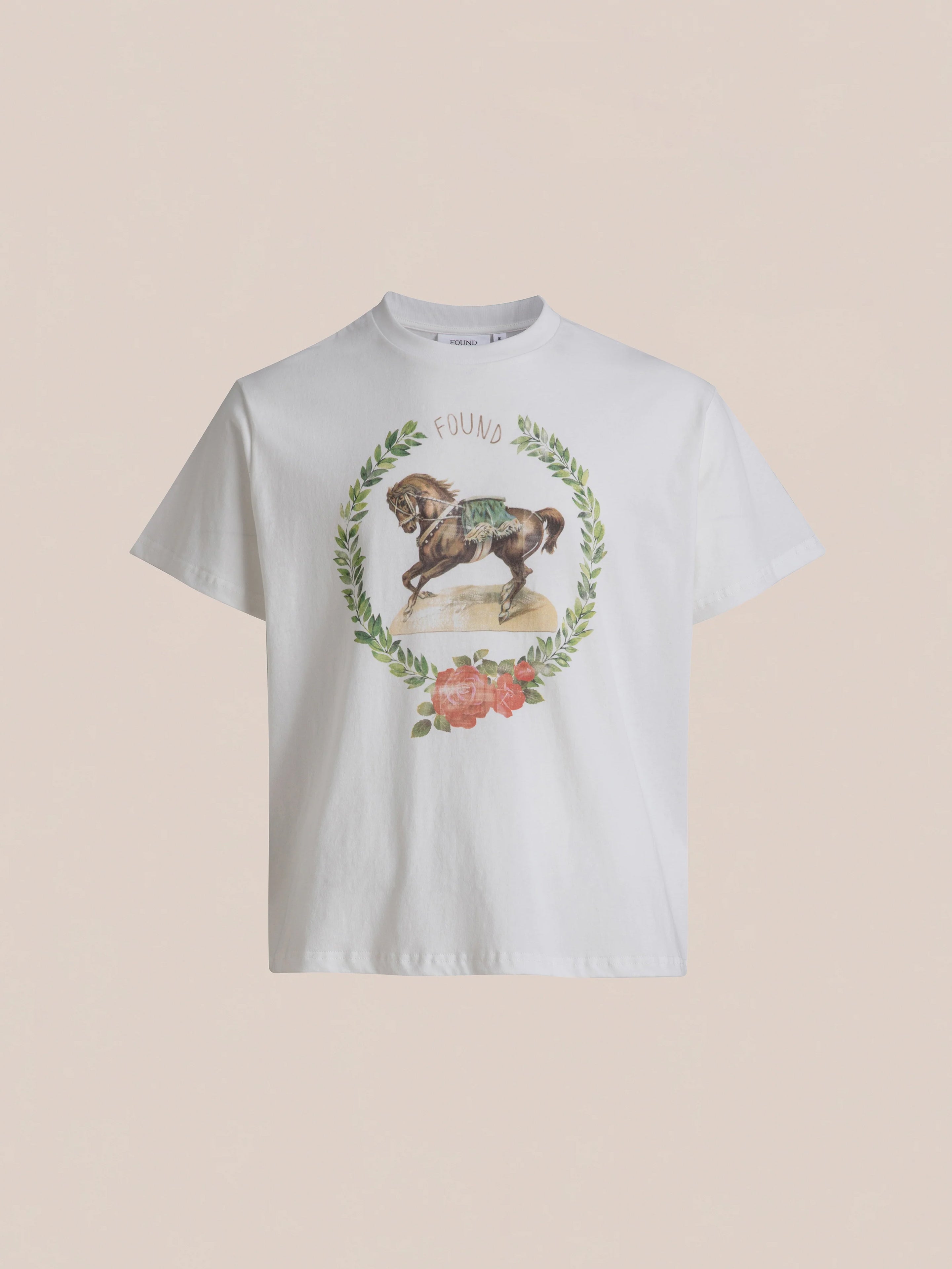 A white Rodeo Tee from the brand FOUND, adorned with a horse graphic encircled by a wreath of leaves and flowers for a vintage feel, and the word "FOUND" printed above the horse.