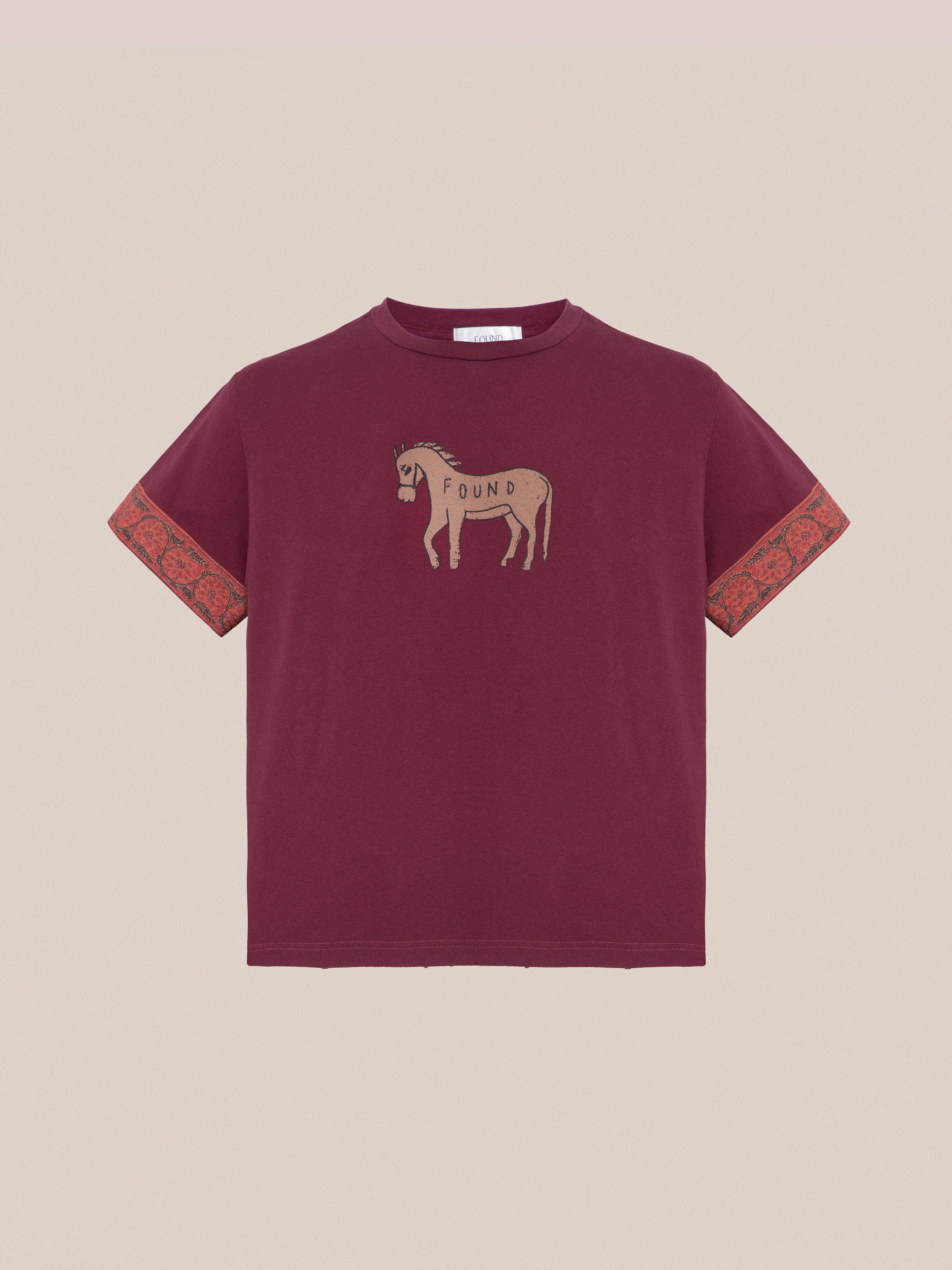 The Horse Embellishment Tee by Found is a maroon T-shirt with a faded purple wash, featuring a donkey graphic and the word "FOUND" on the front. The sleeves are adorned with contrasting patterned red cuffs, adding an extra touch to this casual piece.