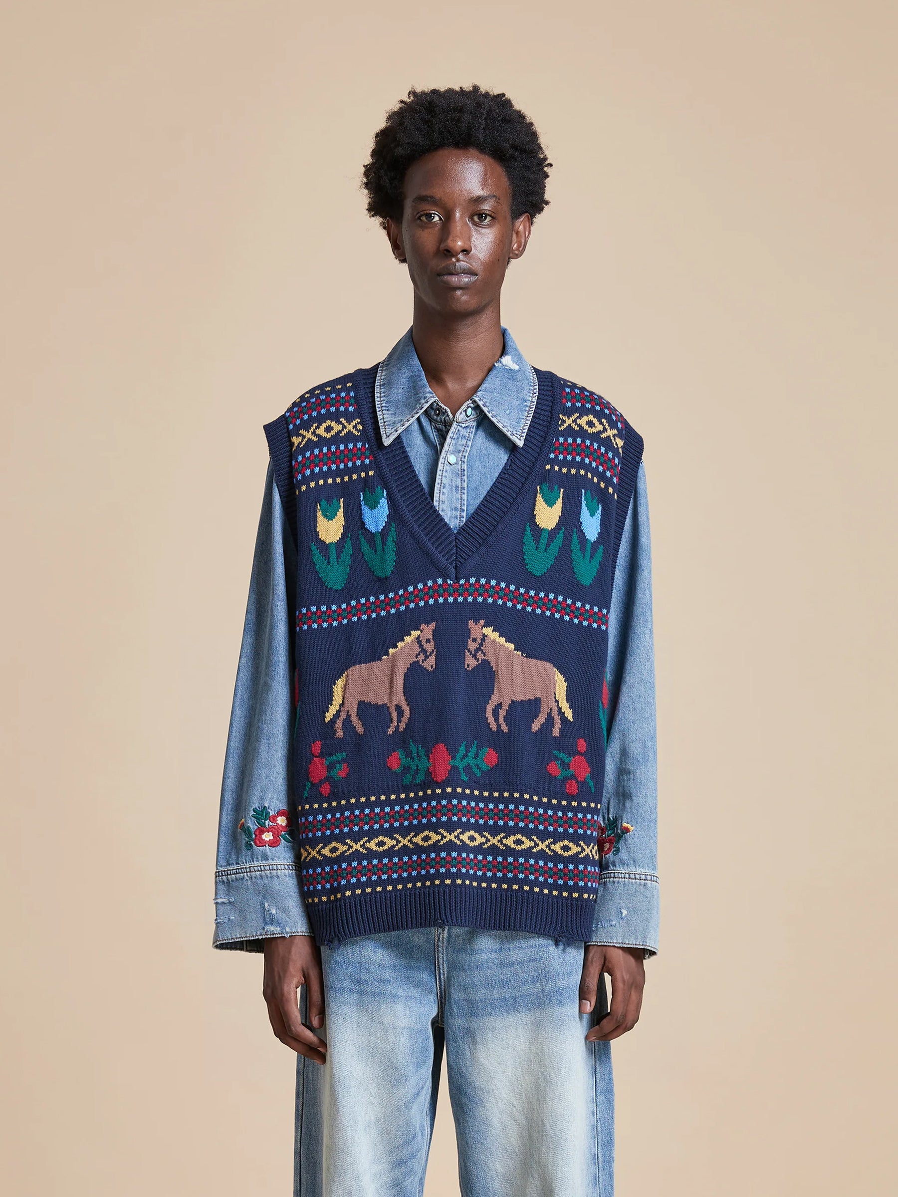 A man wearing the Found Isle Horse Reverie Sweater Knit Vest with South Asian folk art motifs.