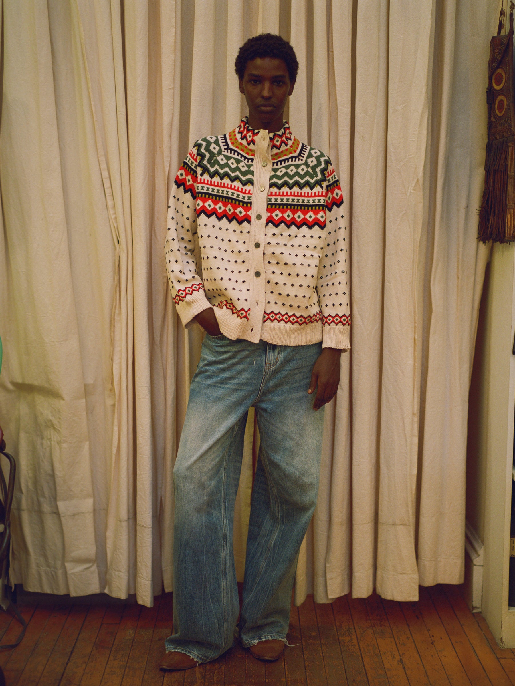 A man in a Found Harwan Isles sweater standing in front of a curtain.