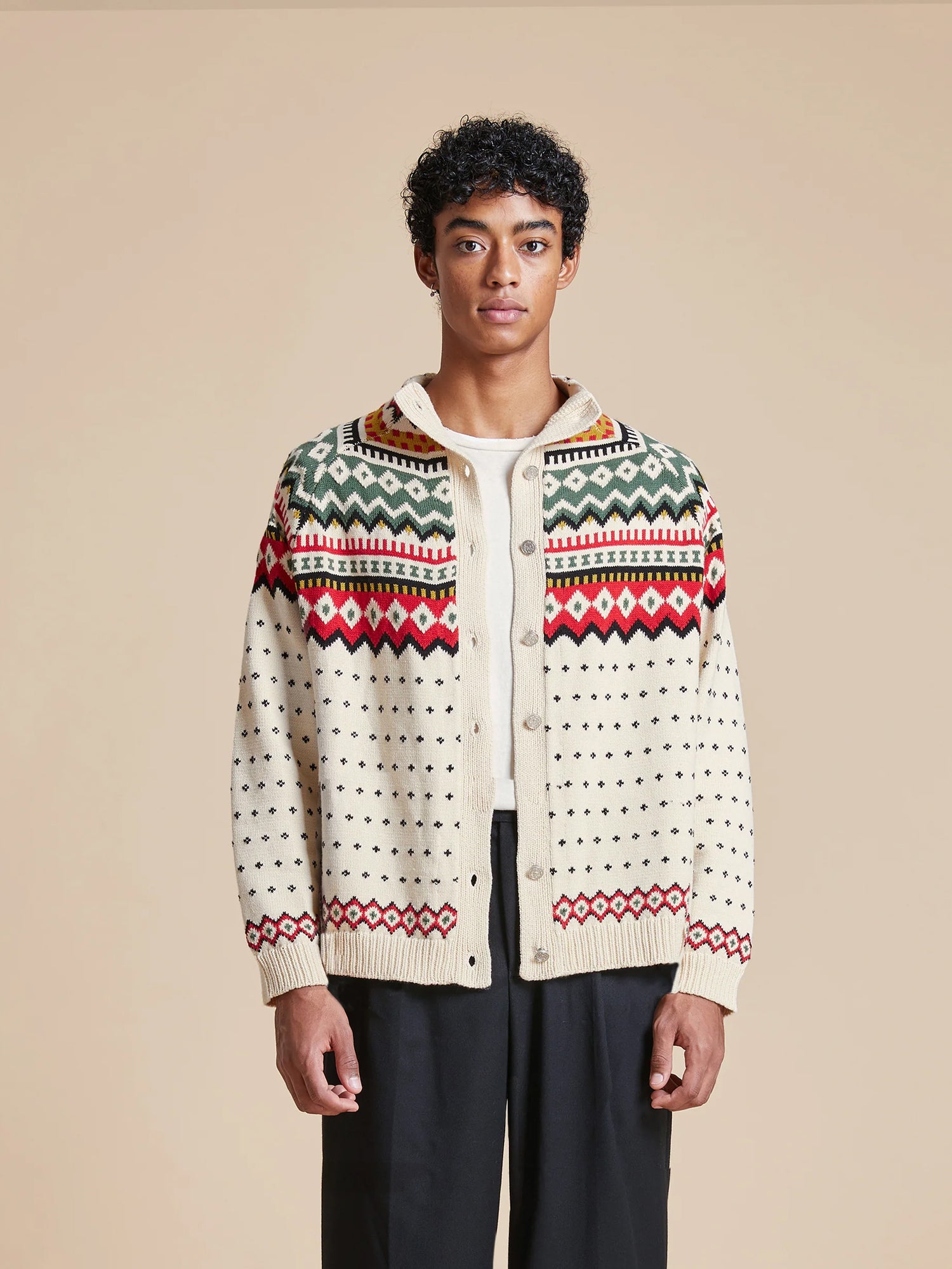 A man donning a Harwan Isles Sweater from Found, a Scottish fair isle knitted cardigan with intricate patterns, paired with trousers.