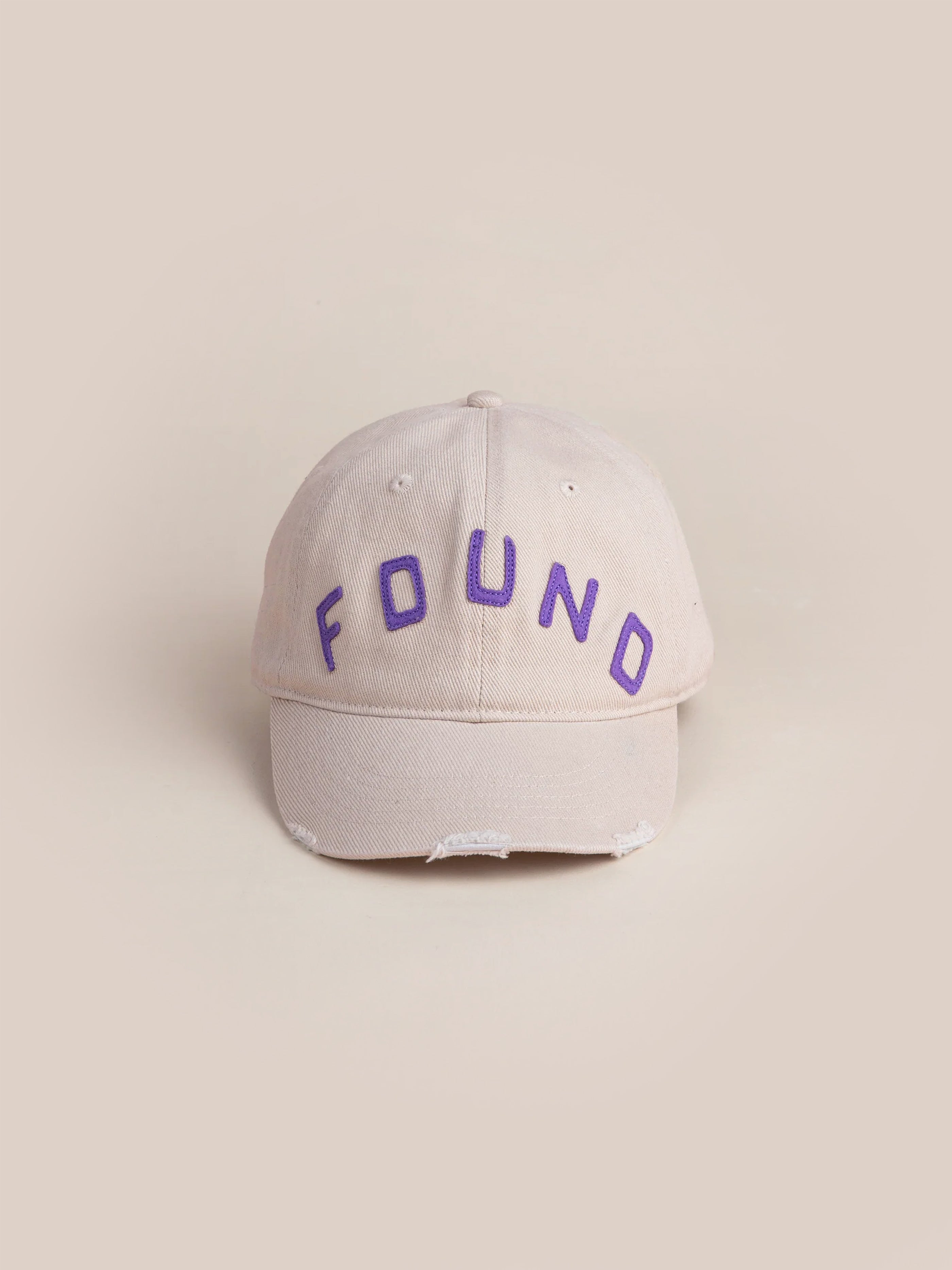 The Ivory Felt Patch Cap by FOUND is a beige baseball cap, made from vintage washed fabric featuring "FOUND" in purple letters on the front, offering a slightly distressed look for an effortlessly stylish addition to any outfit.