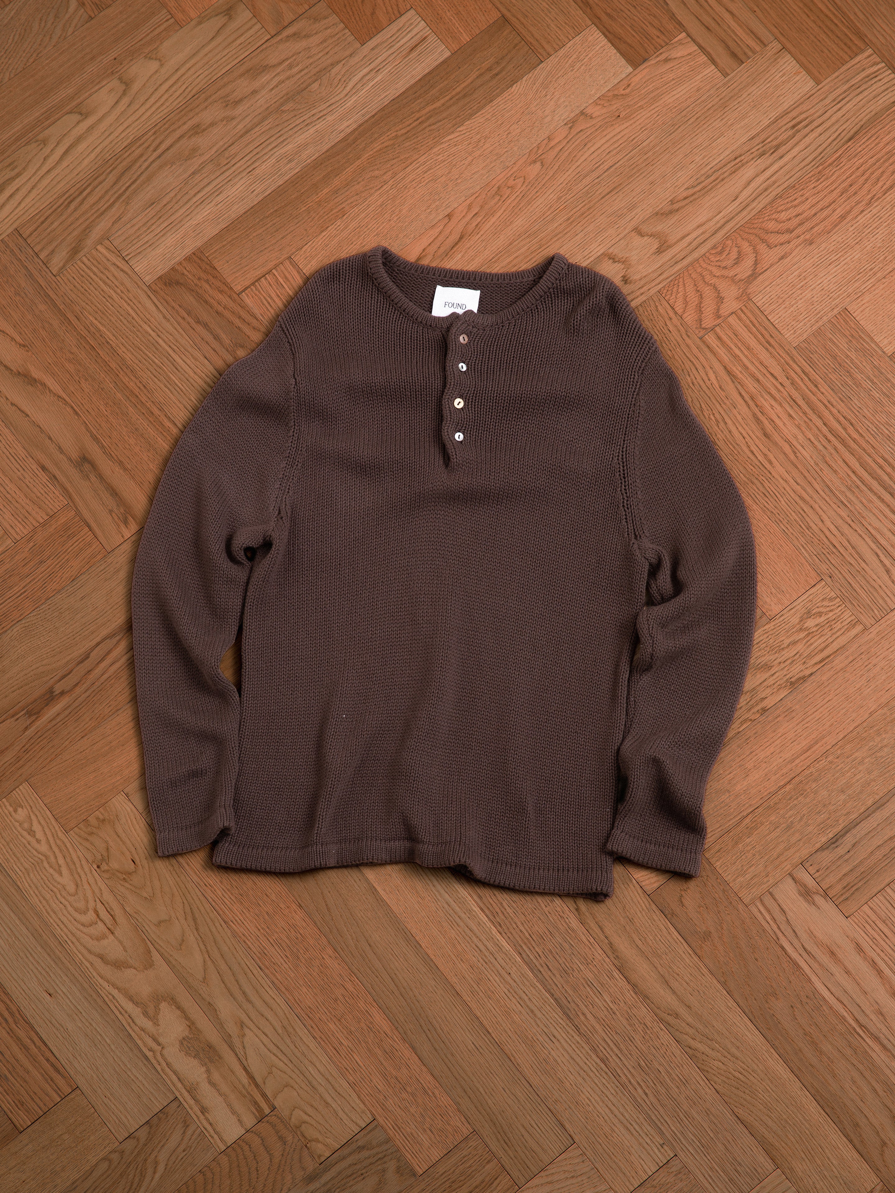 A brown Knit Henley sweater from Profound laying on a wooden floor.