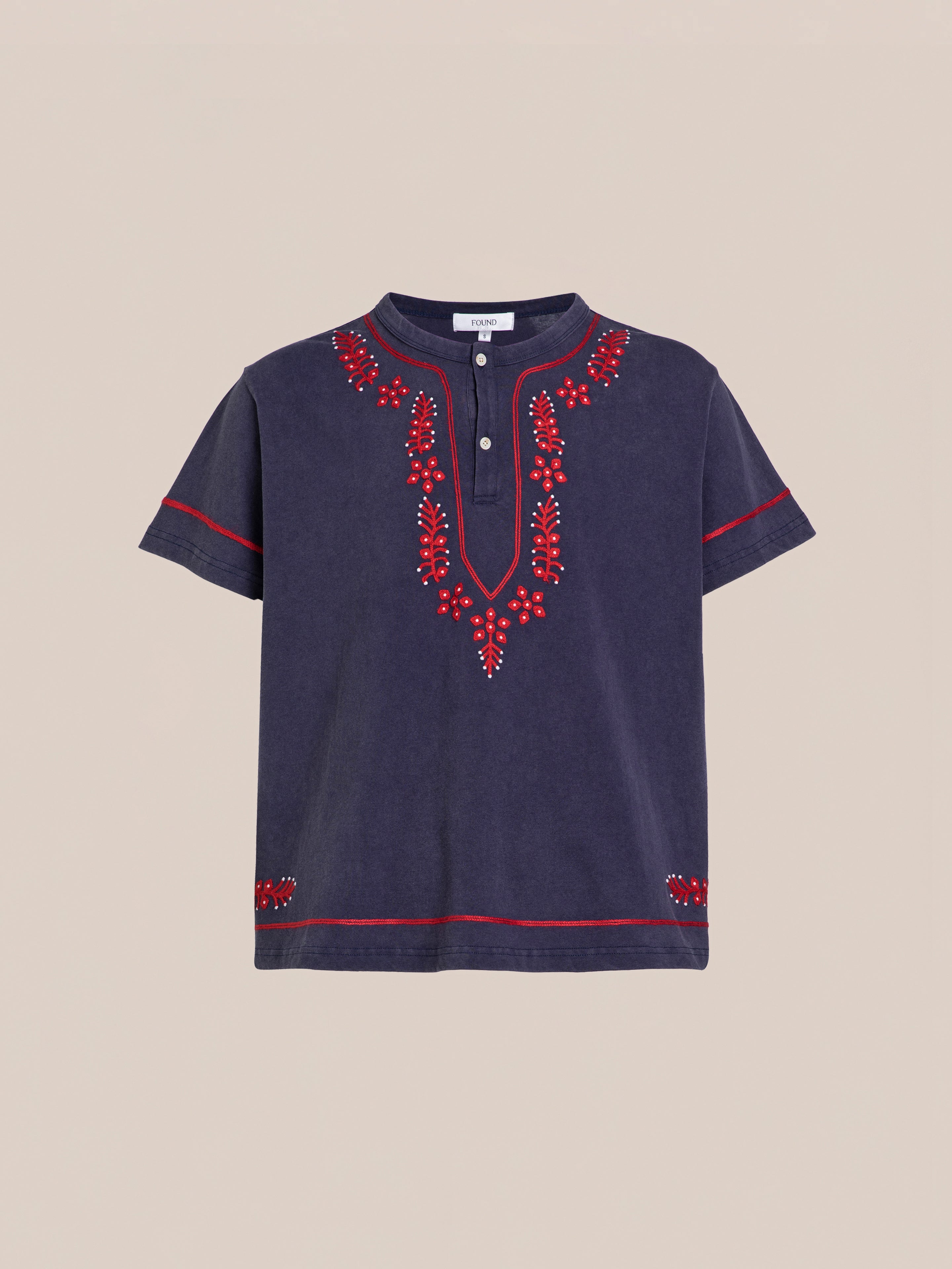 The FOUND Embroidered Henley is a navy short-sleeve shirt with a buttoned neckline, featuring red embroidery along the front, sleeves, and hem.