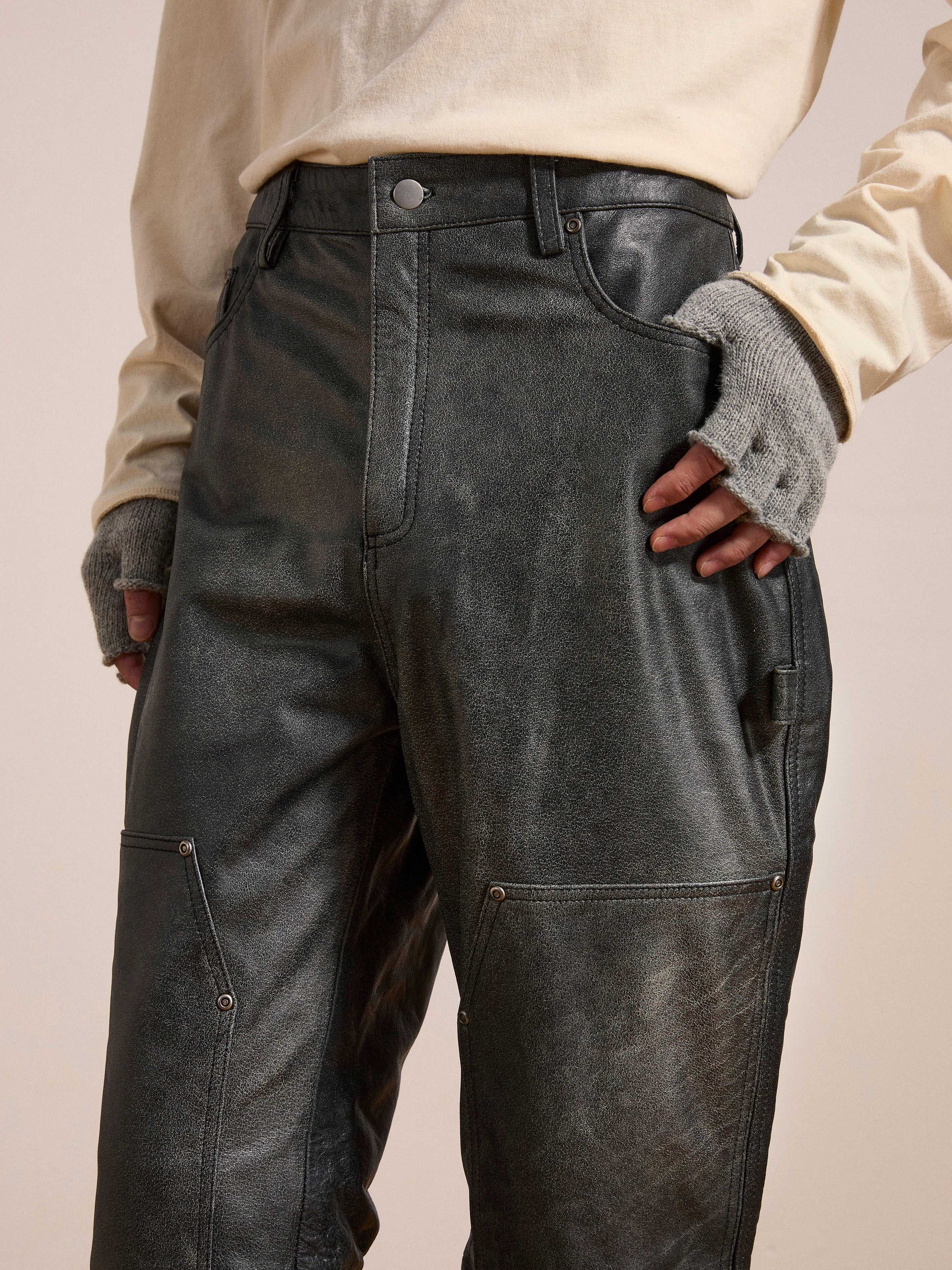 Close-up of a person wearing FOUND Distressed Genuine Leather Carpenter Pants with stitching details, a cream long-sleeve shirt, and gray fingerless gloves. The person's hands are resting on their hips.