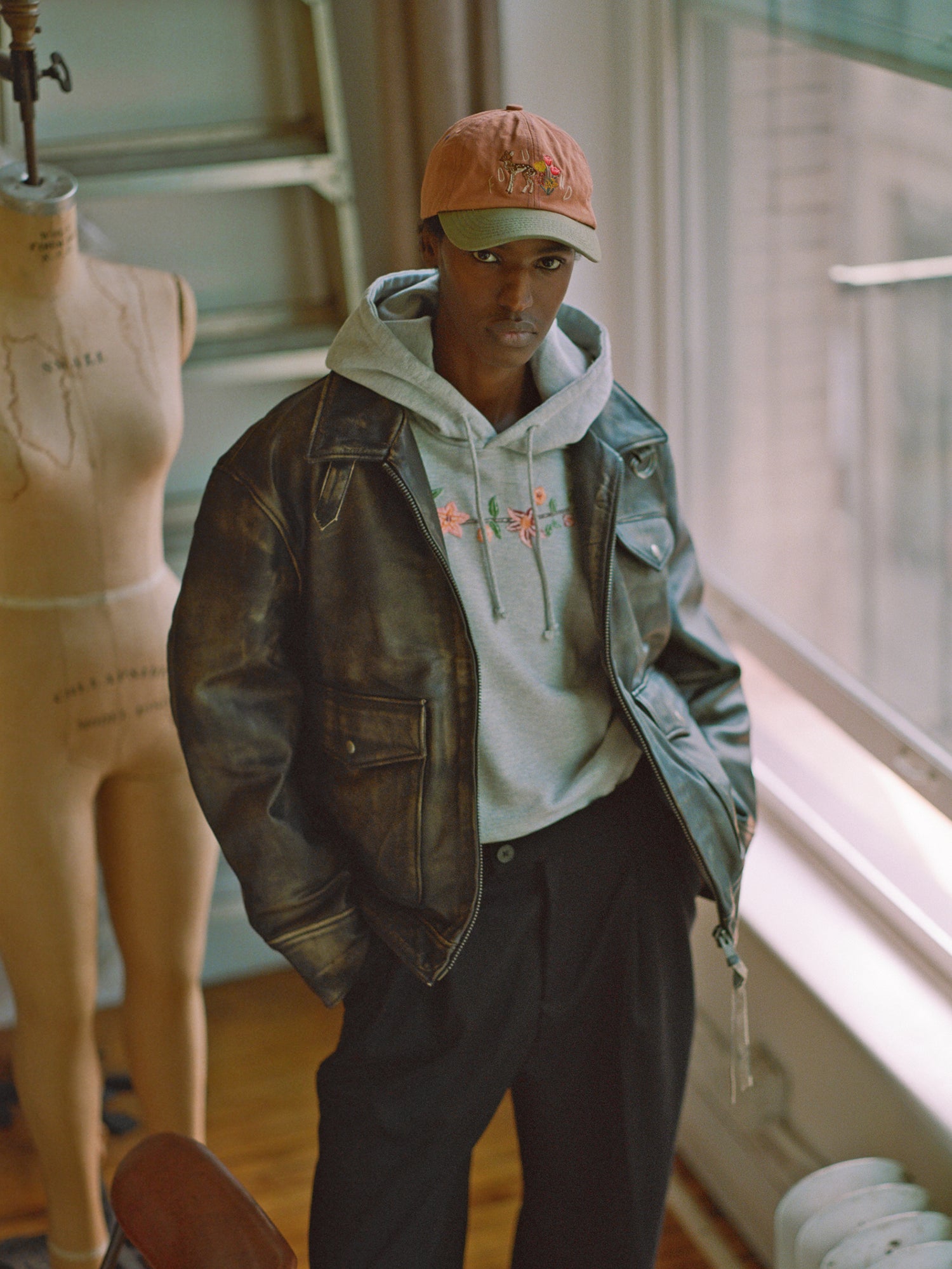 A man in a Found distressed leather pocket jacket and hat standing next to a mannequin.