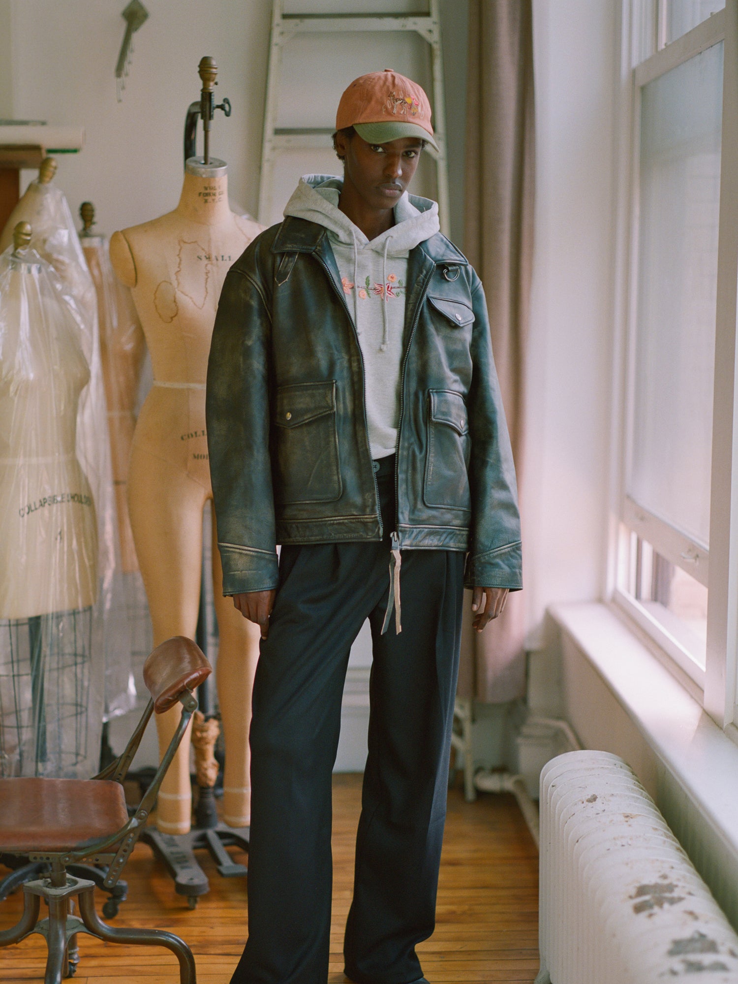 A black man wearing a Found distressed leather pocket jacket stands in front of mannequins in a room.