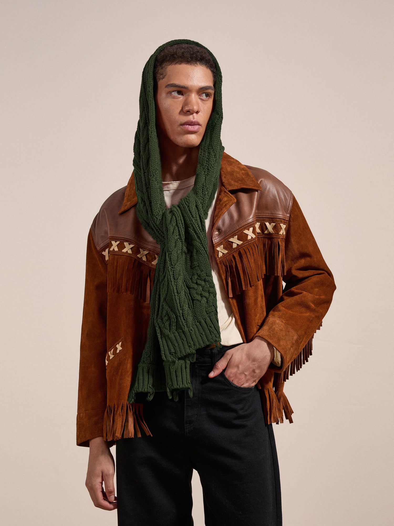 A person wearing a brown fringe jacket, white shirt, black pants, and the FOUND Forest Distressed Cable Knit Scarf over their head looks off to the side against a neutral background.