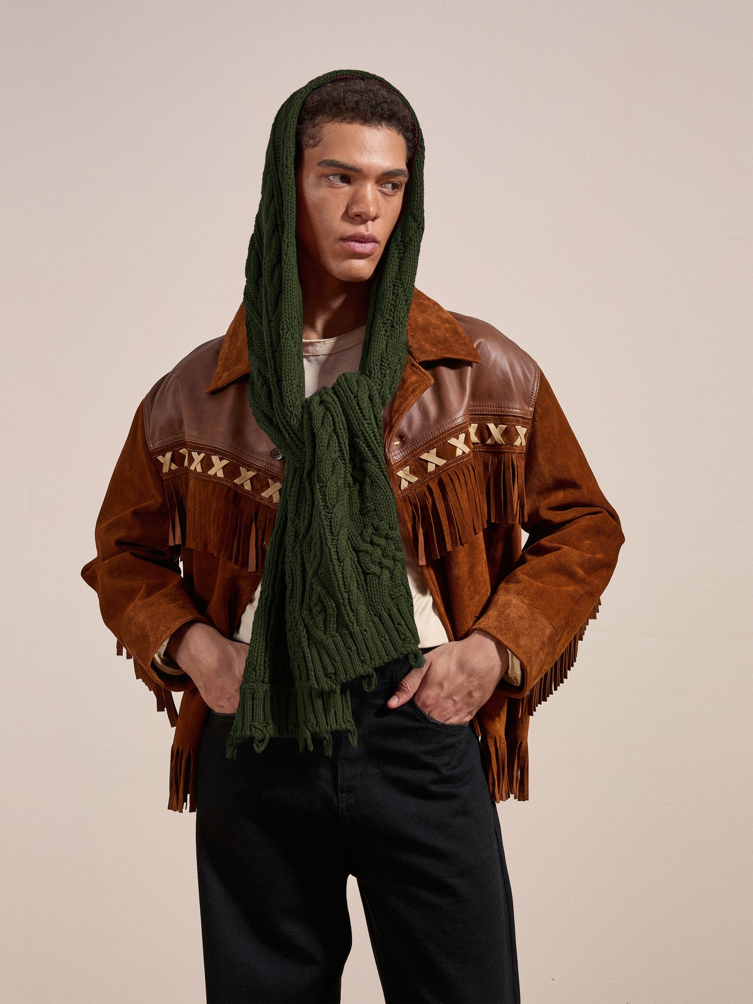 A person wearing a brown fringed jacket over a beige shirt, along with the FOUND Forest Distressed Cable Knit Scarf, stands against a plain background.