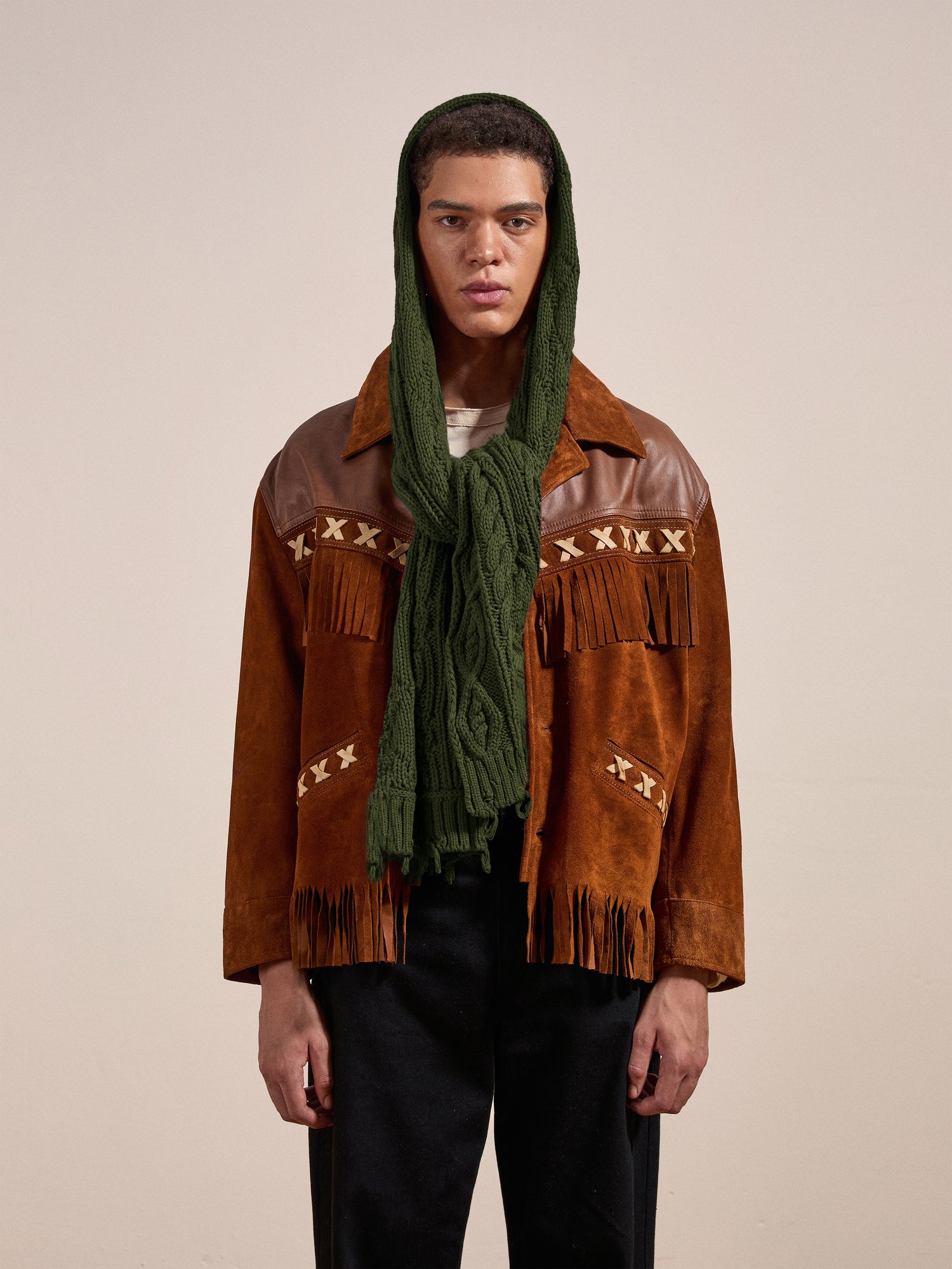 A person wearing a brown suede jacket with fringe details and a Forest Distressed Cable Knit Scarf from FOUND over their head stands against a plain backdrop.