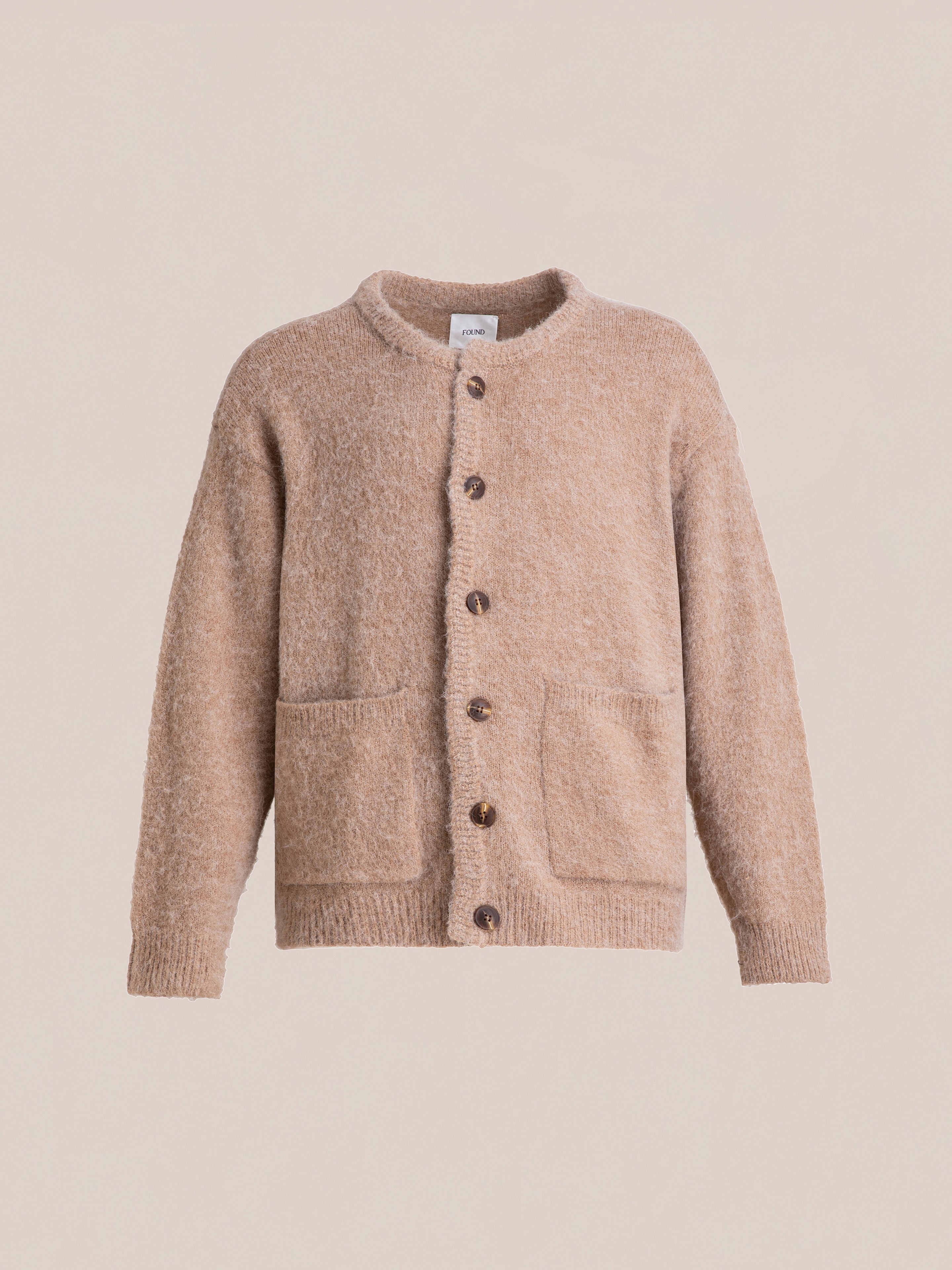 A beige, button-up Mohair Cardigan by FOUND with an oversized fit and tortoise buttons, featuring two front pockets, displayed against a plain light background.