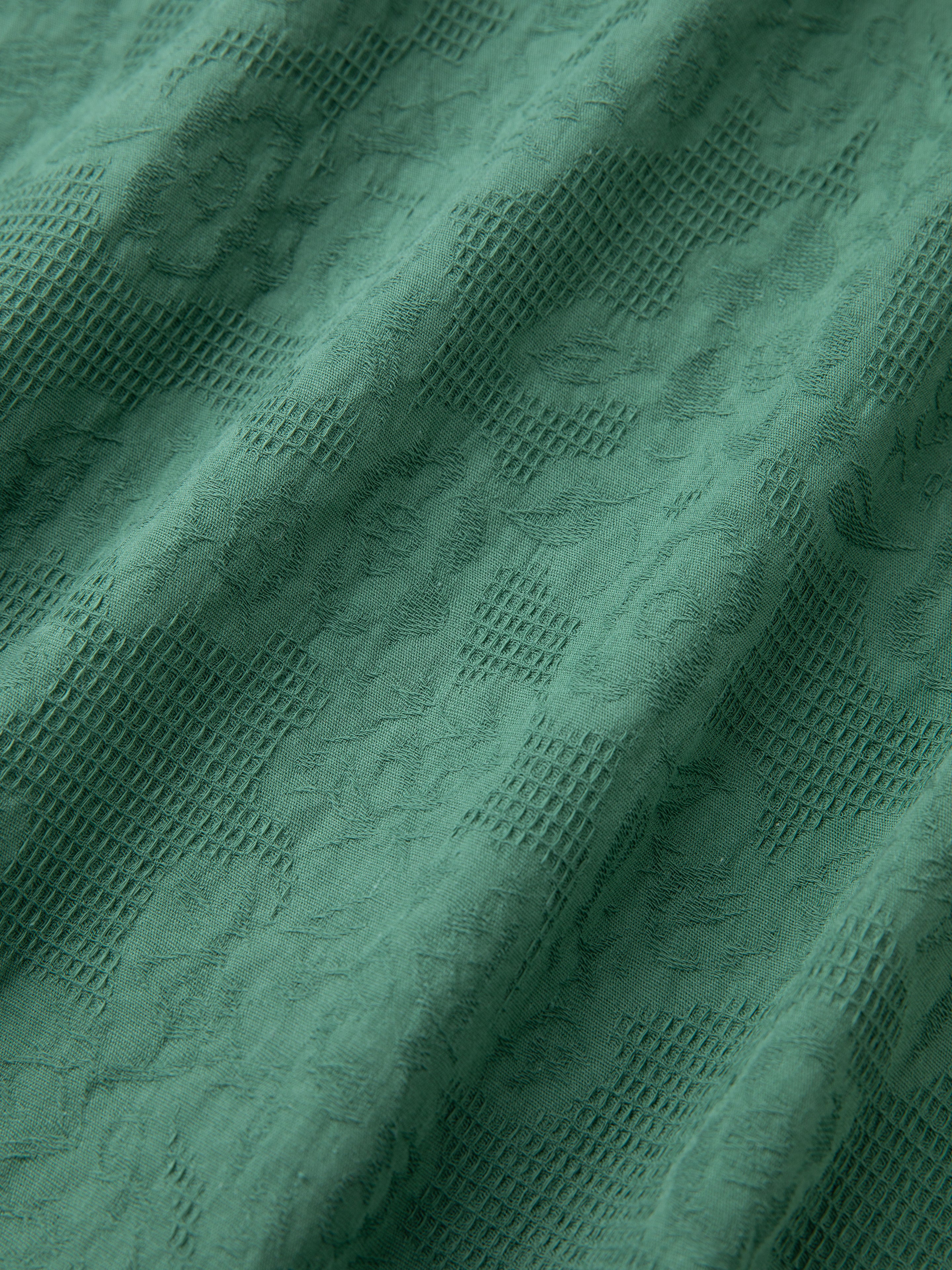 A close-up of green fabric with a textured floral pattern and mesh-like design, reminiscent of the intricate lace detailing often found on a Found Mount Camp Shirt.