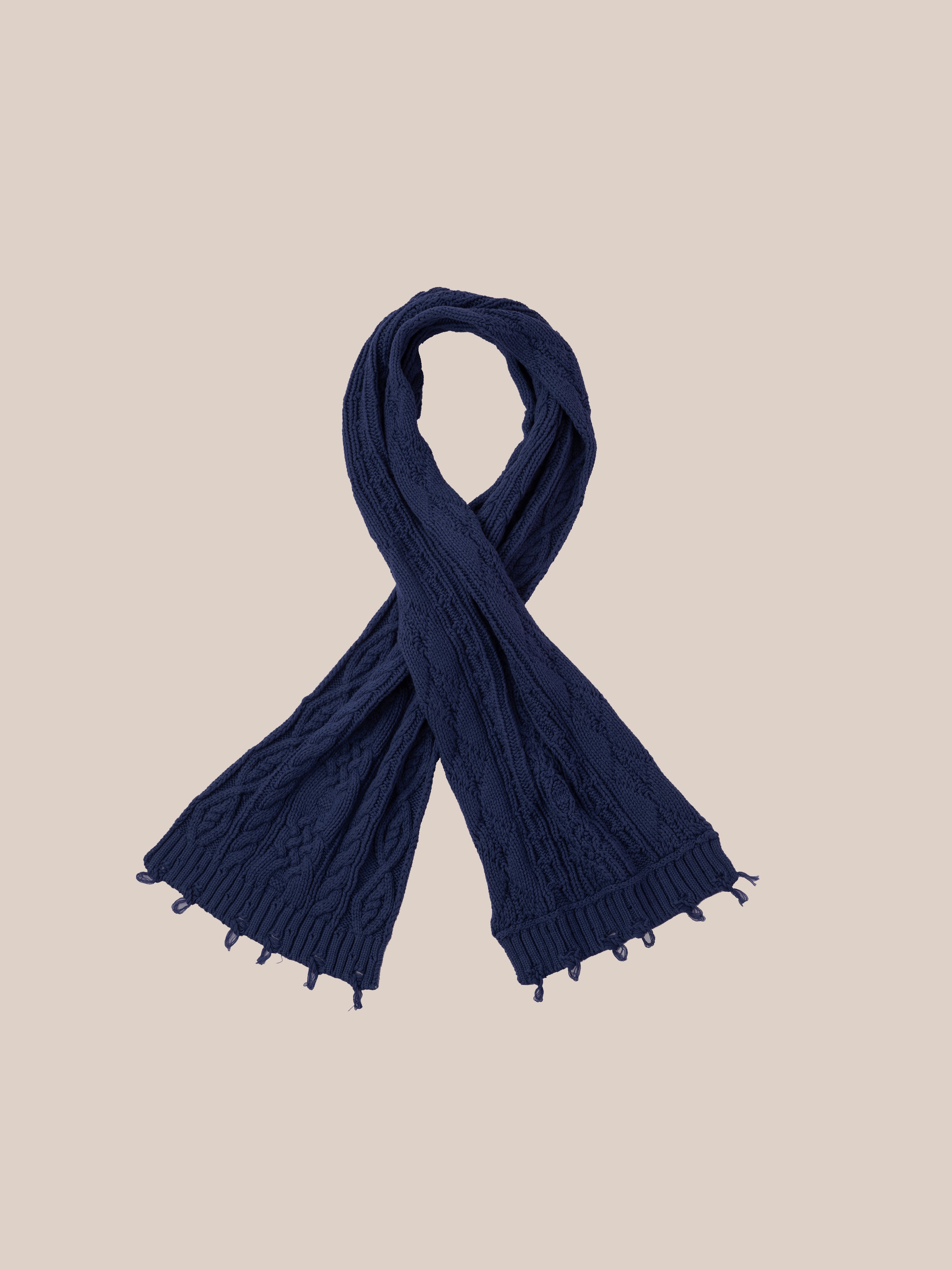 A Navy Distressed Cable Knit Scarf from FOUND, featuring a textured pattern, laid out on a neutral beige background.