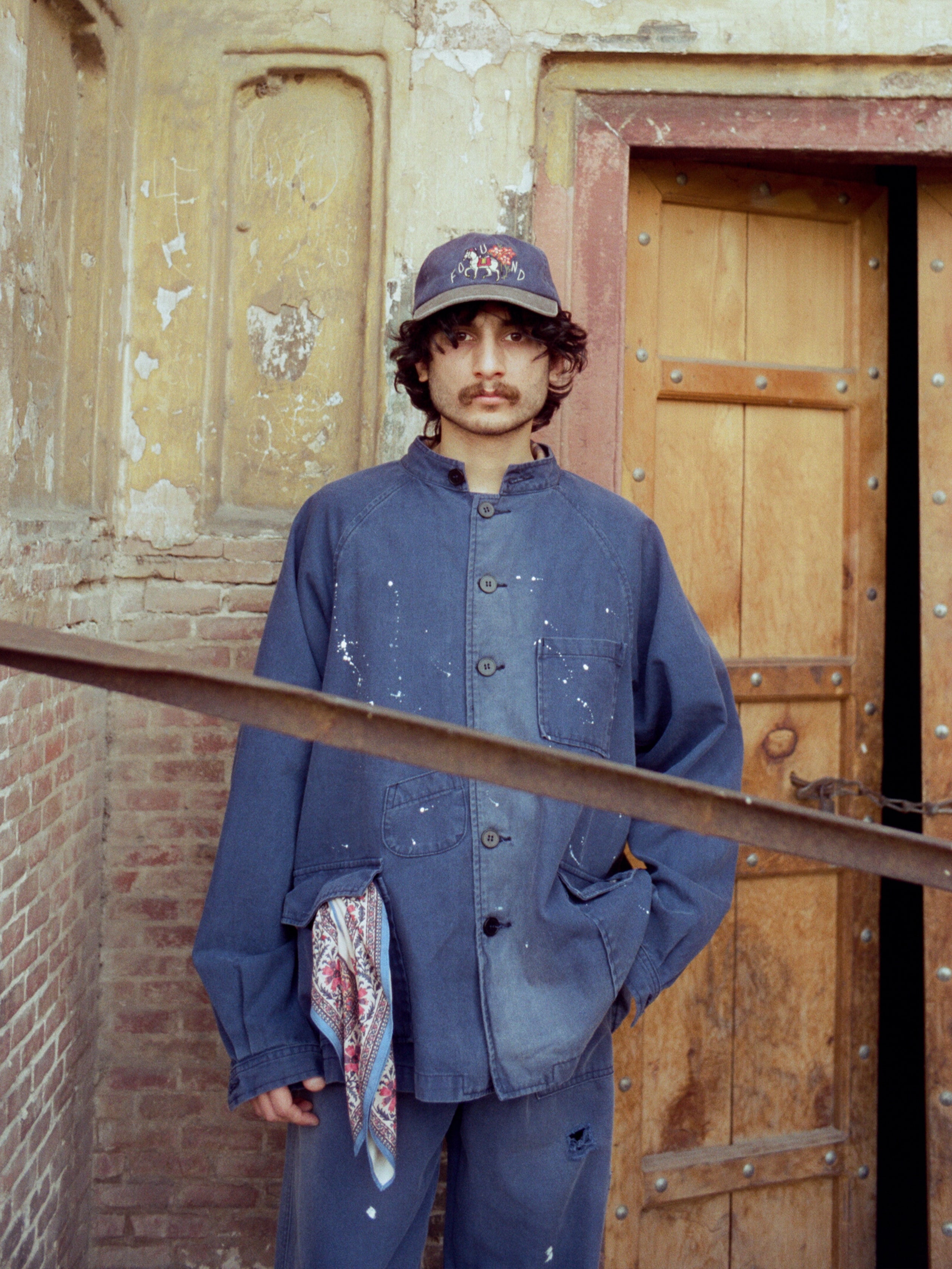 A man in a Found River Painters Chore Coat, with form-fitting shoulders, standing next to a wooden door.