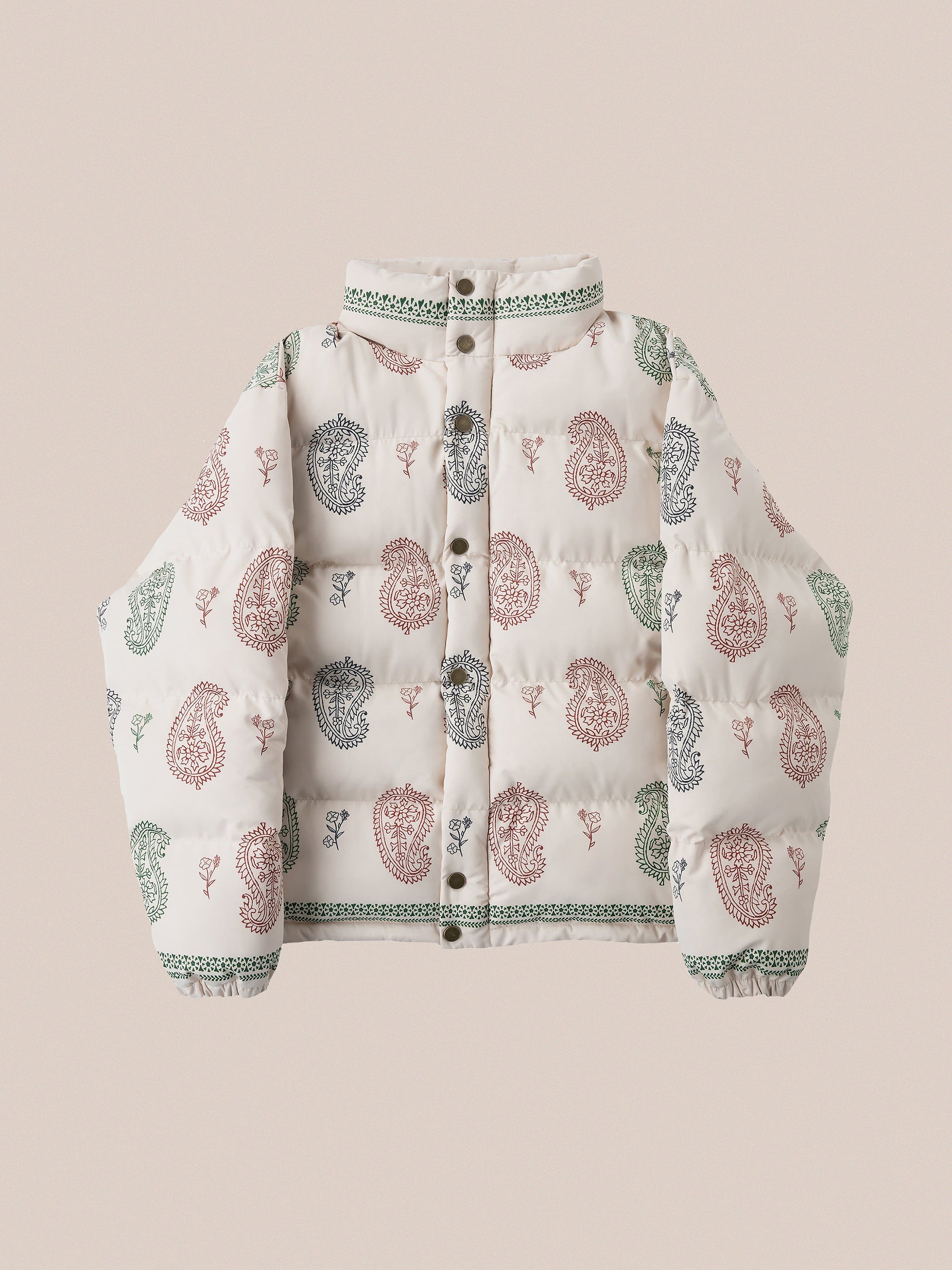 The Paisley Puffer Jacket in Cream by FOUND features traditional red and green paisley patterns on a cream background reminiscent of a bandana, equipped with buttons, a collar, and adjustable waist toggles for an ideal fit.