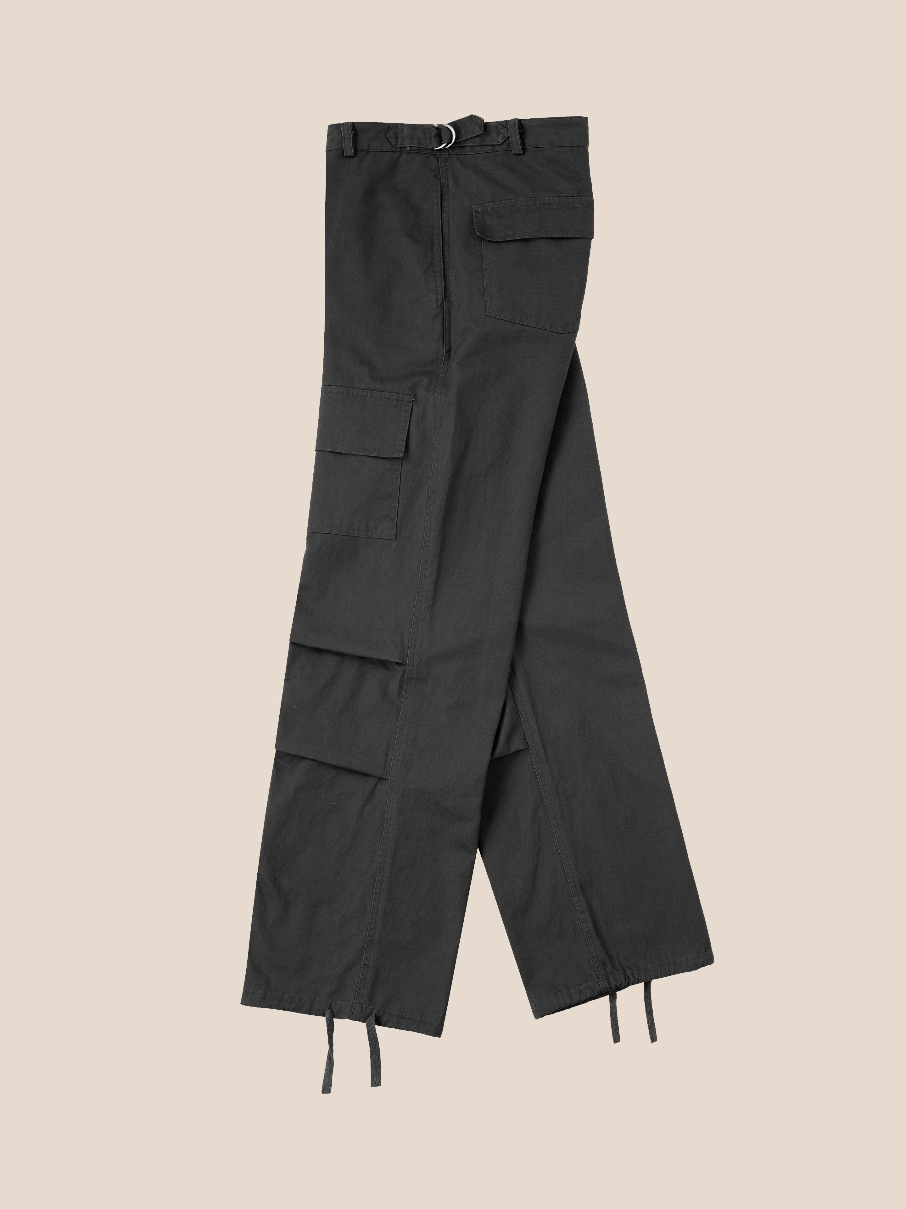 A pair of Parachute Cargo Twill Pants by Found, featuring multiple pockets, an adjustable waist, and drawstring hems in black, folded and placed on a beige background.