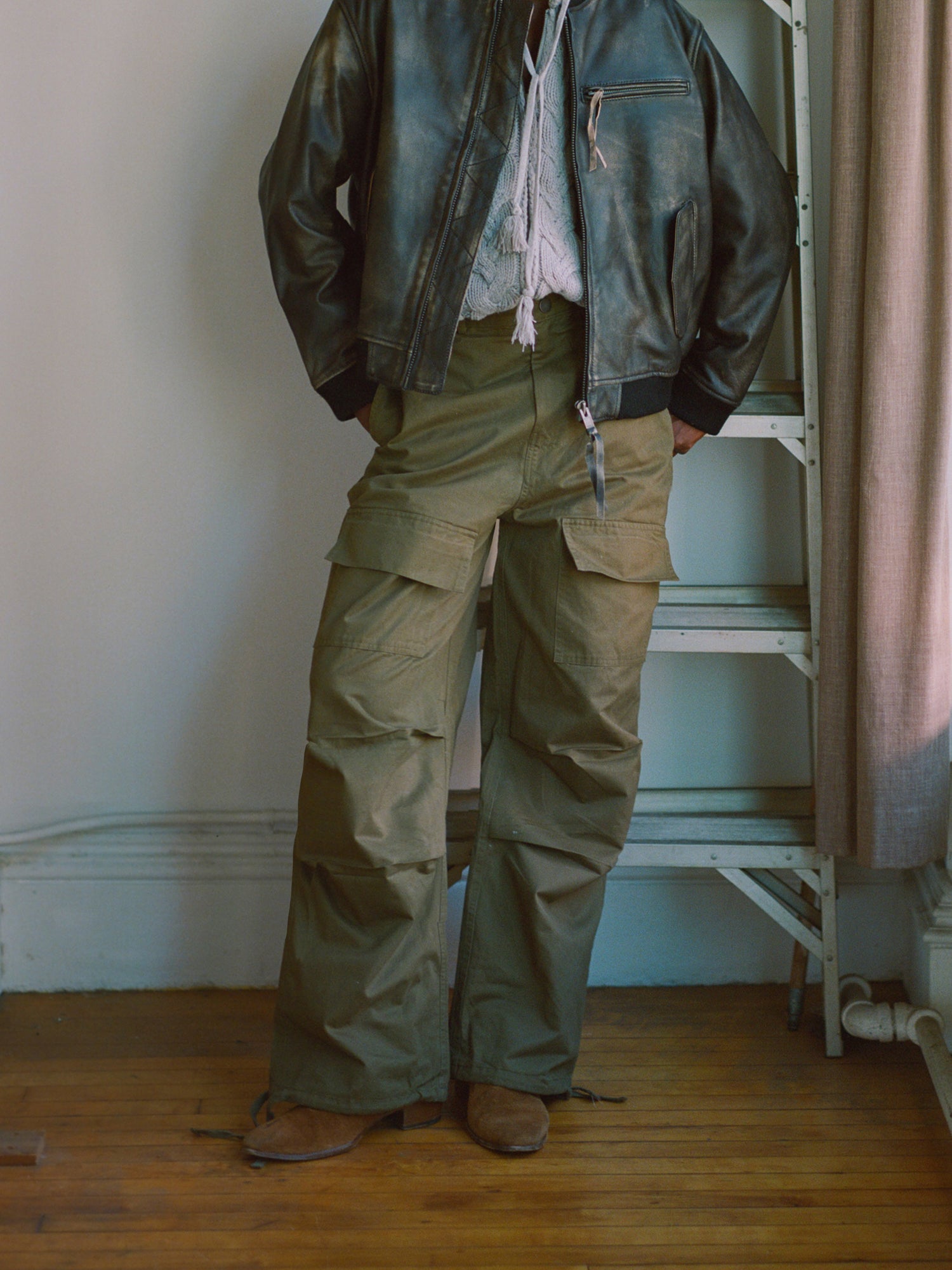 A man wearing Found Parachute Cargo Twill Pants and a leather jacket standing next to a ladder.