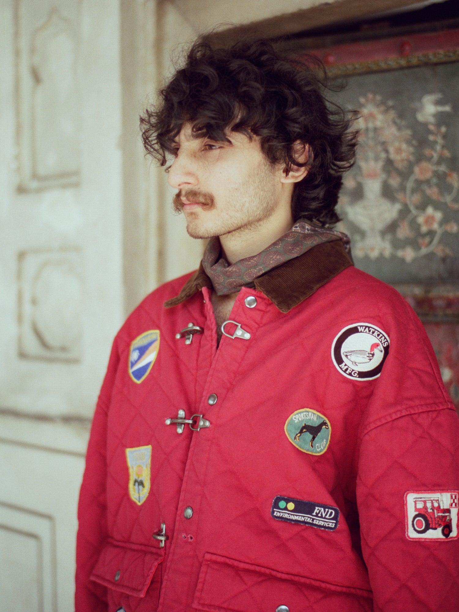 A man wearing a Found Farmstead Quilt Patch Jacket with patches on it.