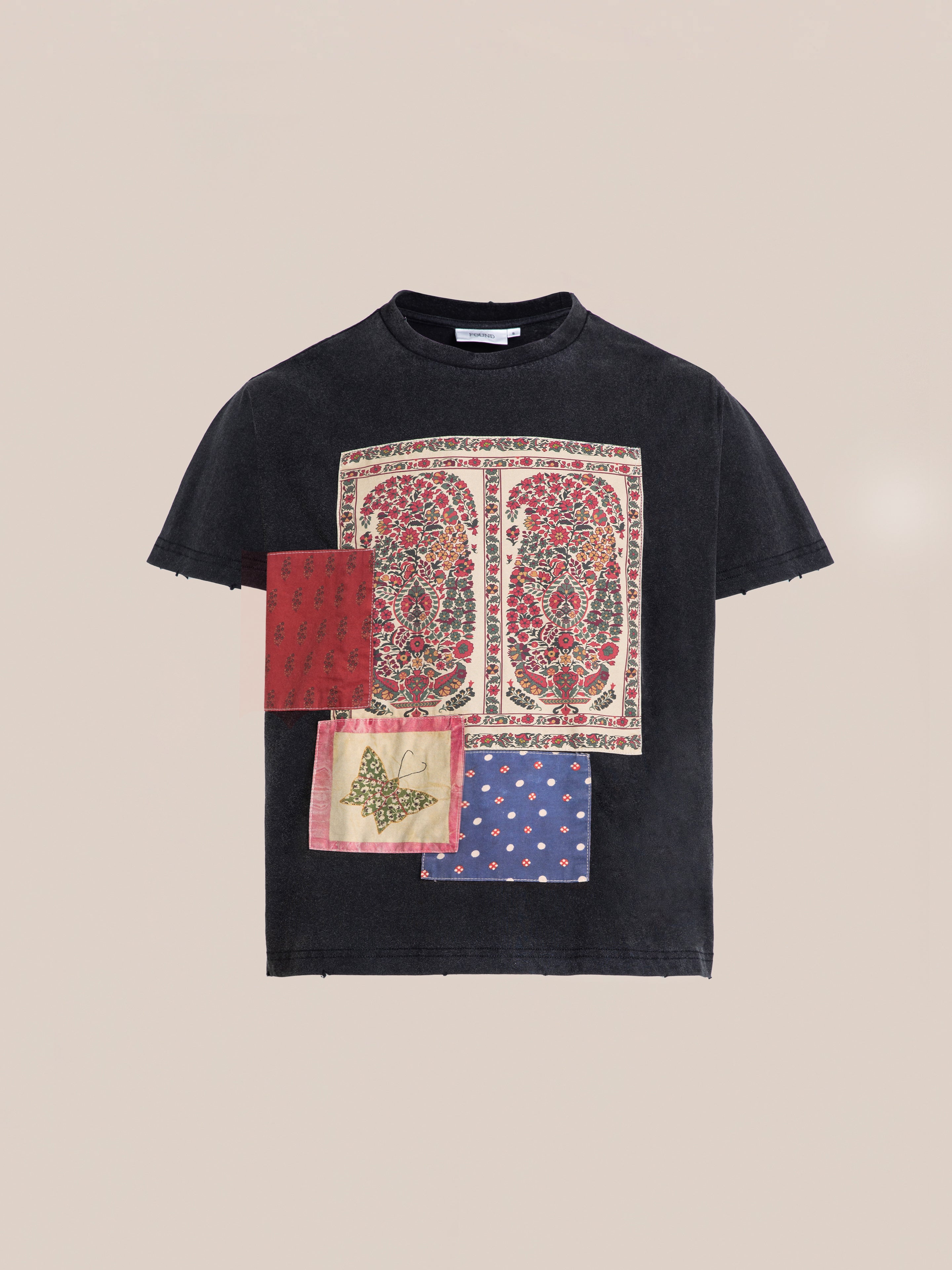 Introducing the Patchwork Tee by FOUND – a black t-shirt showcasing an intricate printed design on the front, which includes two rectangular ornate paisley patterns and three smaller patches with diverse patterns and a butterfly motif, all set against a plain background.